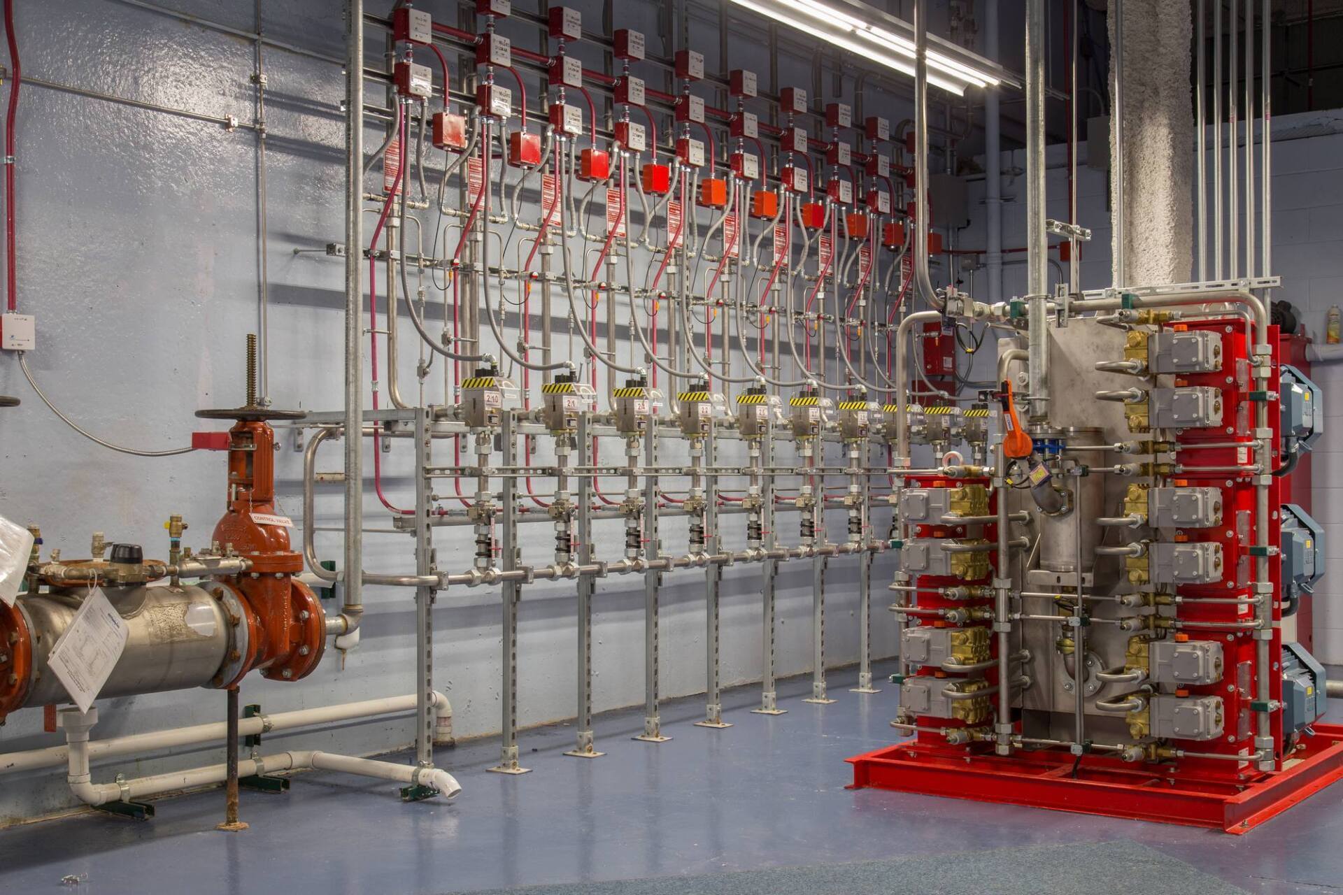 Pipes and valves in a utility room. Red and silver equipment against a gray wall, red base.