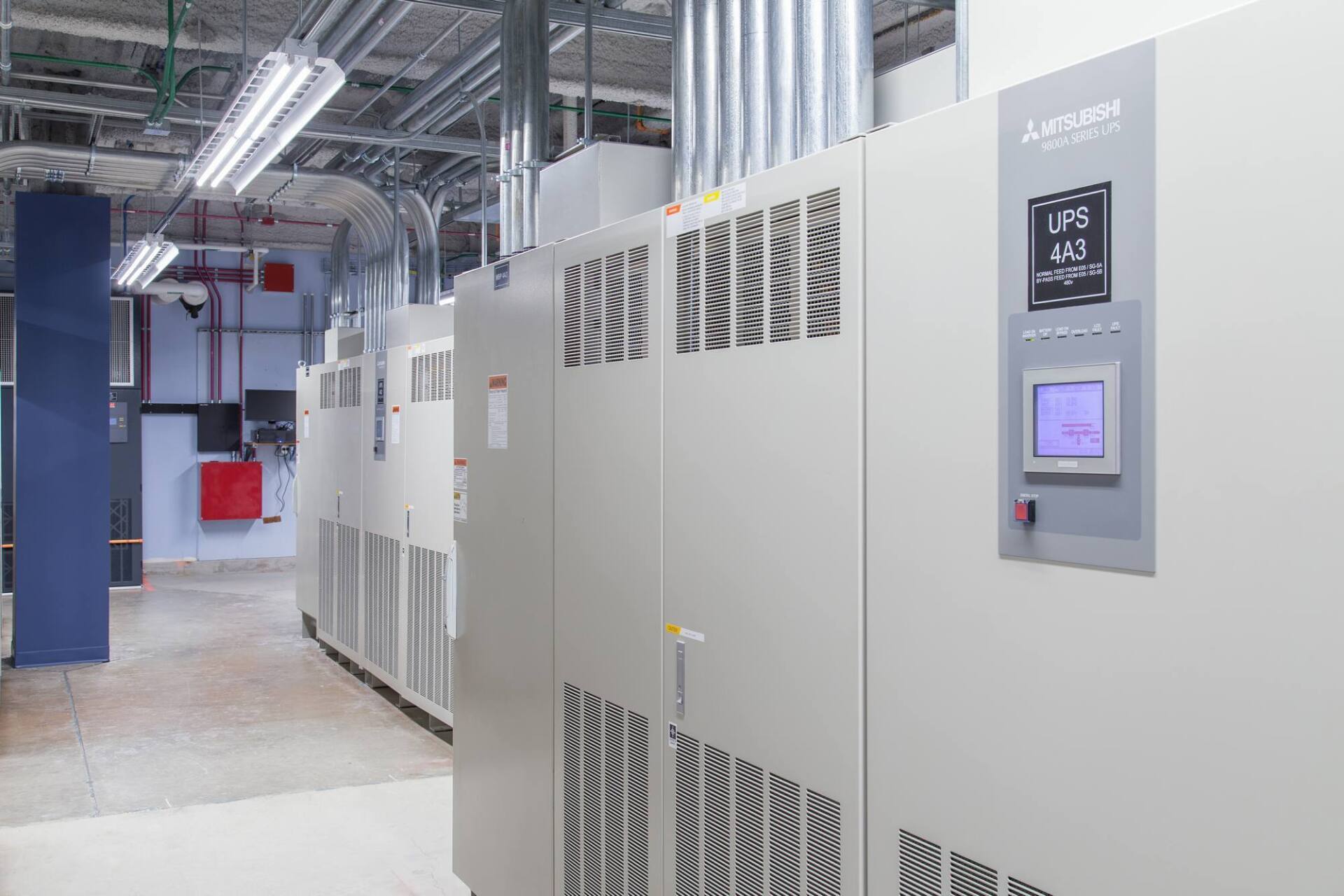 Row of industrial cabinets in a facility, with displays and ventilation grilles; fluorescent lights overhead.