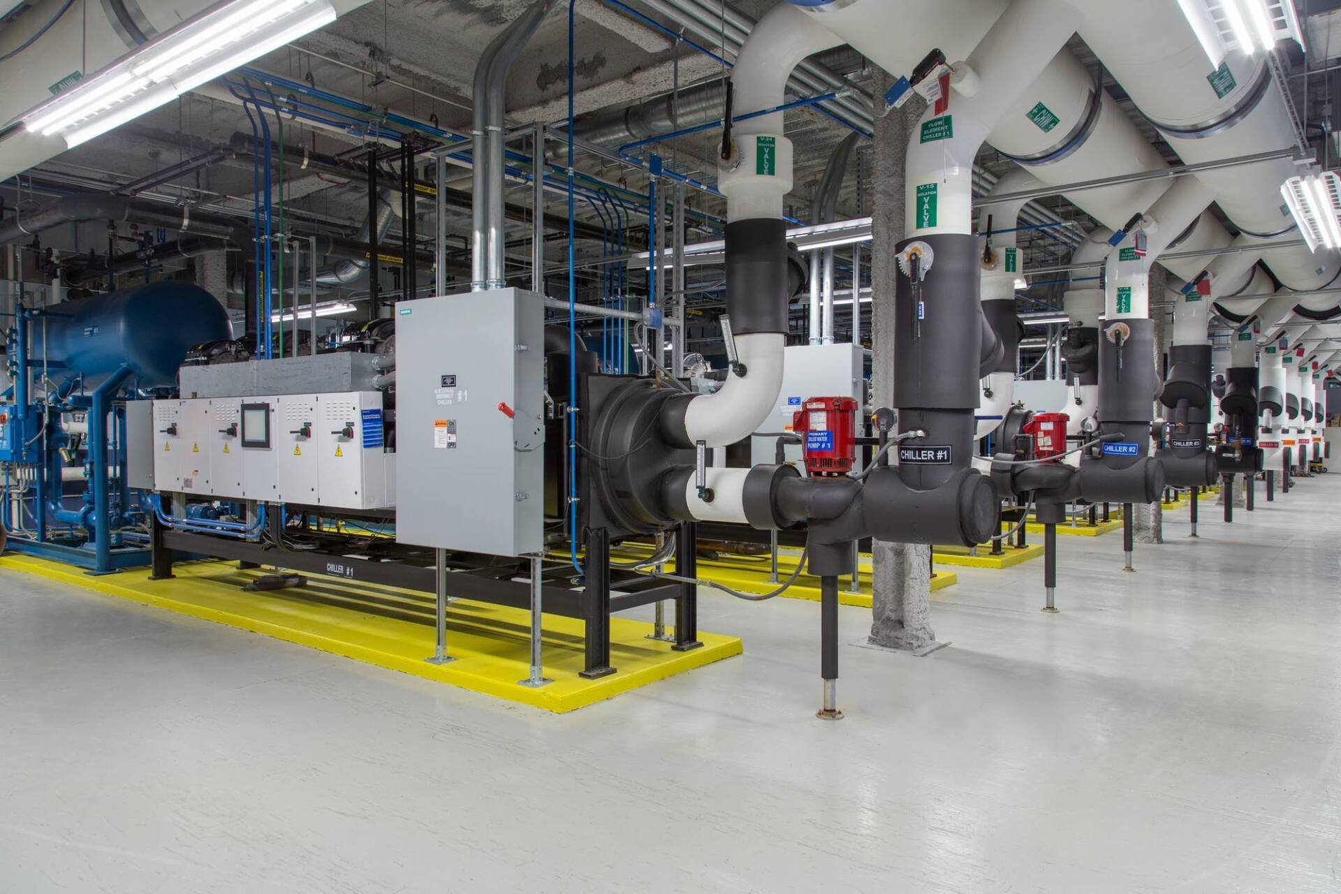Industrial equipment room with pipes, valves, and electrical components. White, blue, and black colors.
