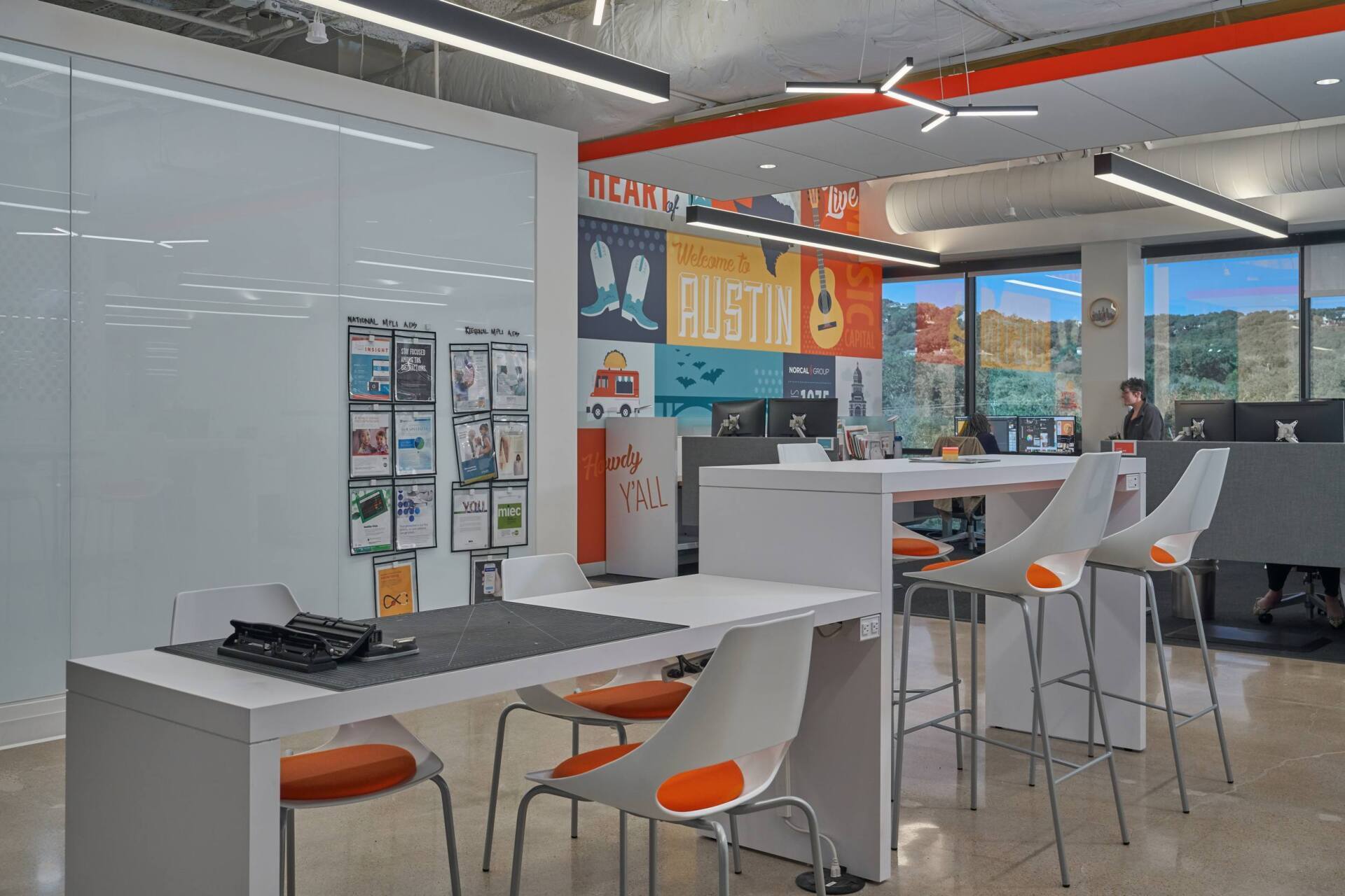 Modern office interior with white tables and chairs, a mural, and orange accents.