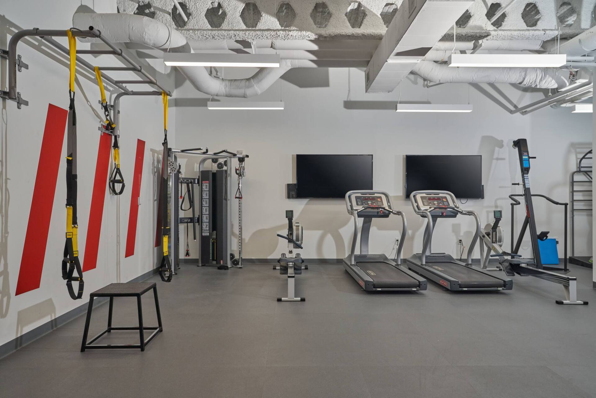 Gym interior with exercise equipment, including treadmills, weight machines, and a TRX system.