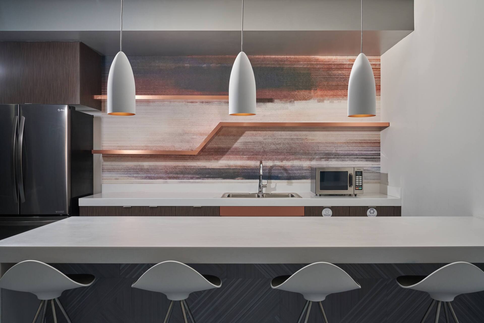 Modern kitchen with white countertops, bar stools, pendant lights, and decorative backsplash.