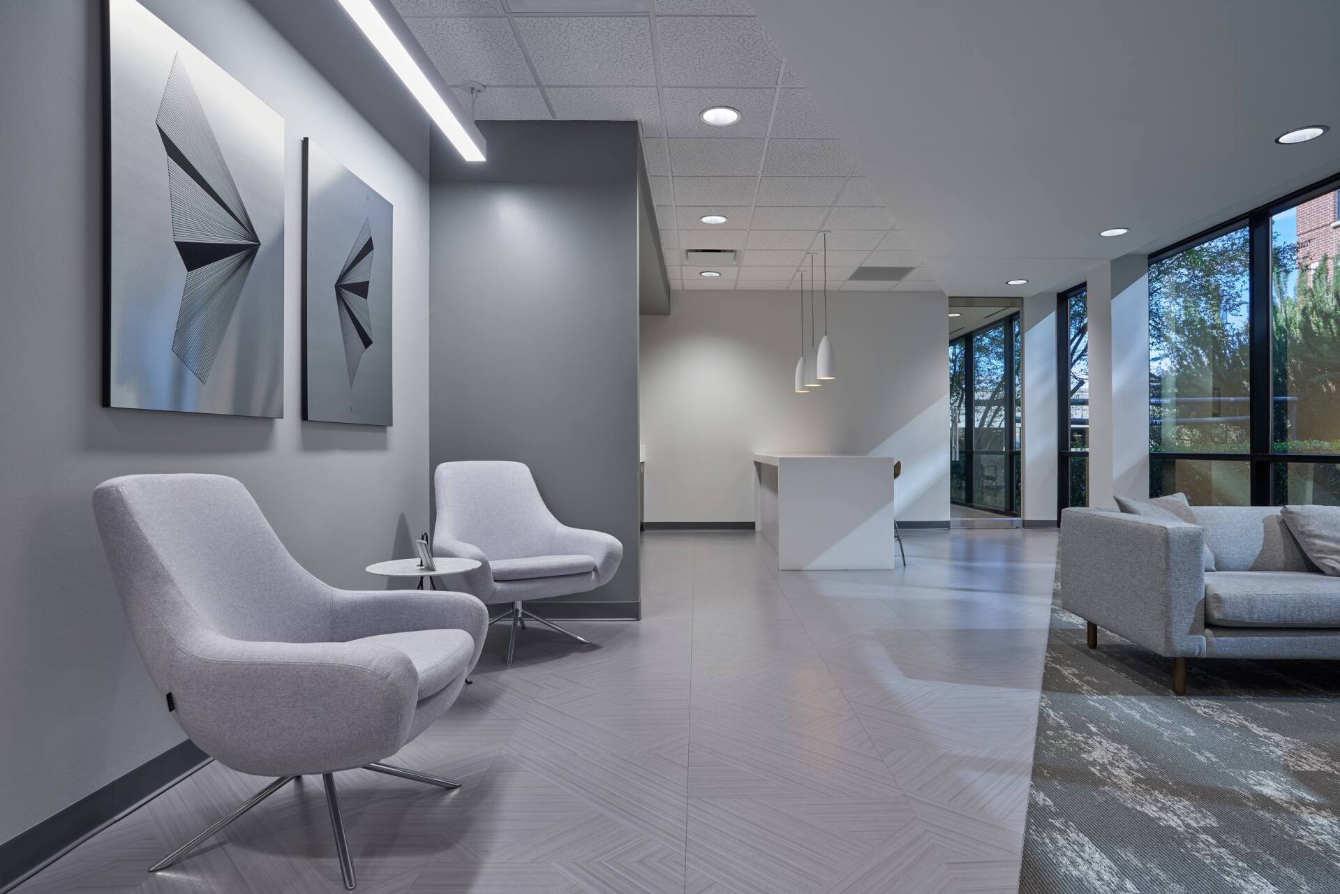 Modern waiting room with gray walls, chairs, art, and windows.