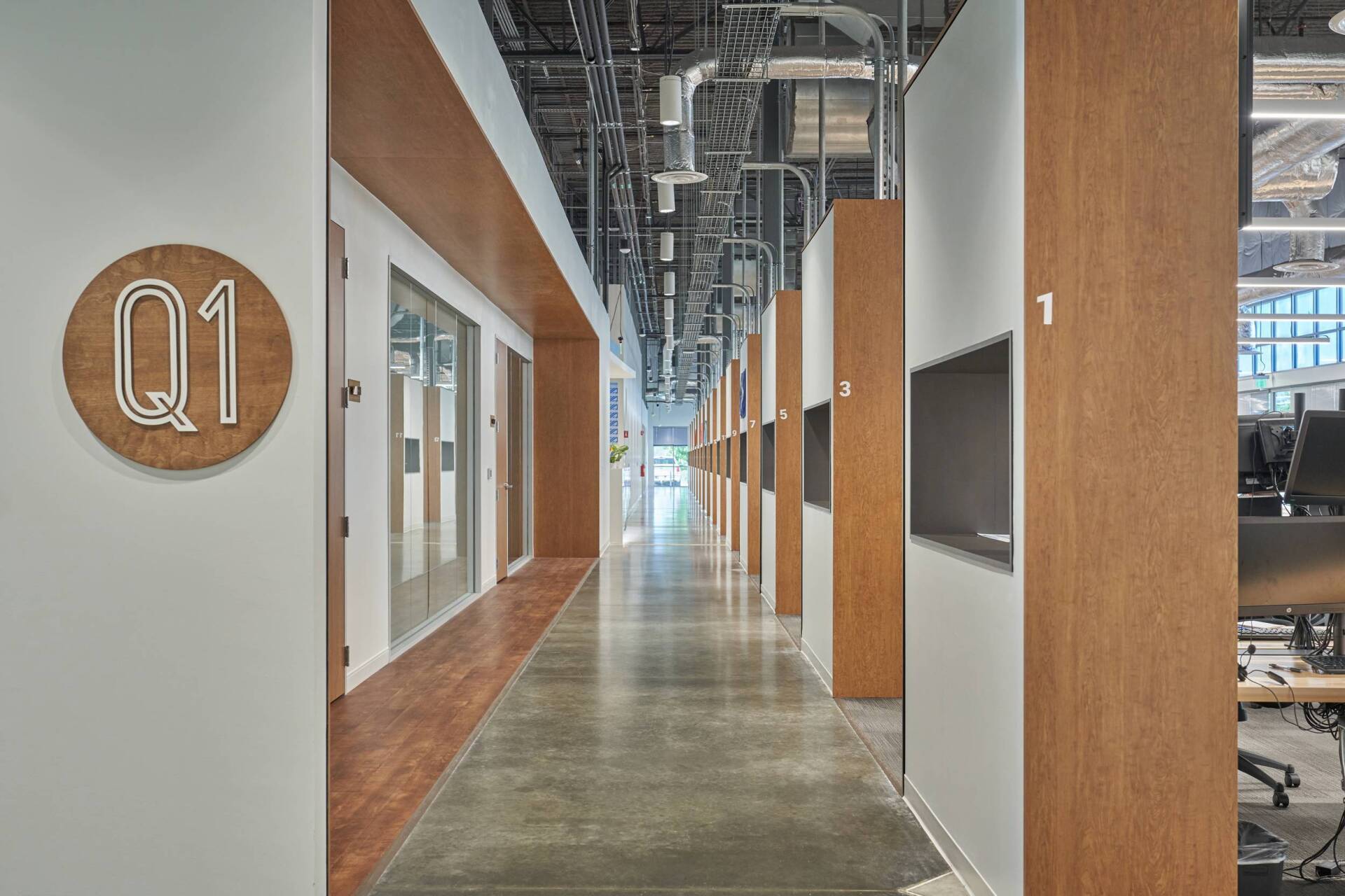 Office hallway with wooden accents, gray concrete floor, and overhead industrial elements.