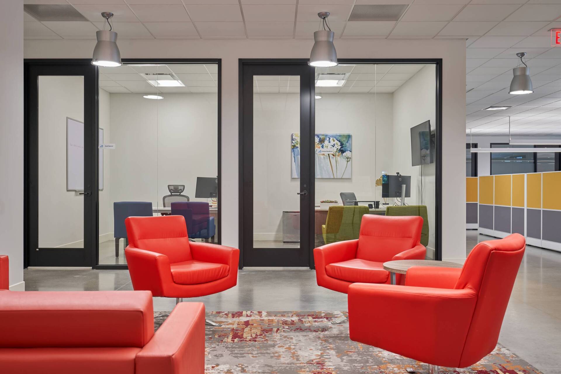 Office waiting area with red seating, glass-walled offices, and pendant lights.