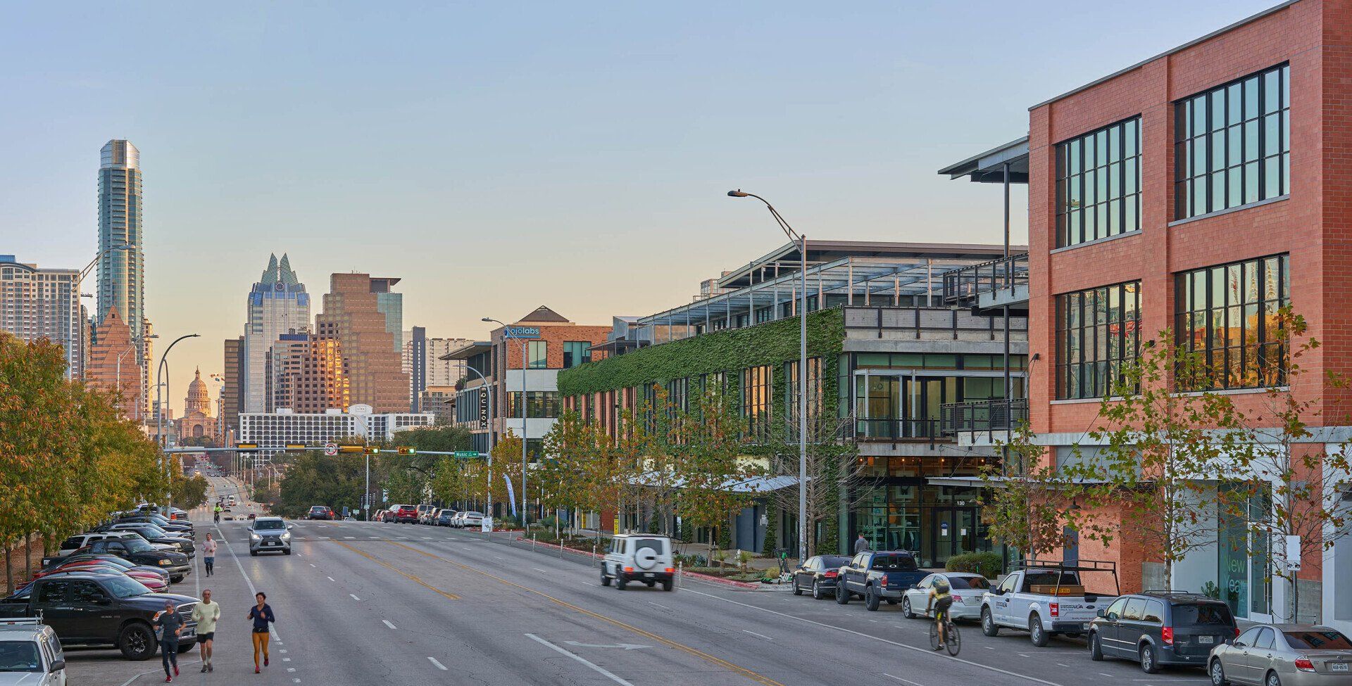 Street view in Austin, Texas, with buildings, cars, pedestrians, and skyline in background.