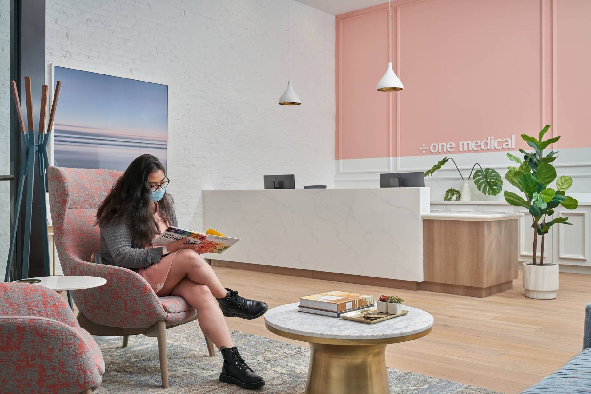 Woman wearing a mask reads in a waiting room with modern décor.
