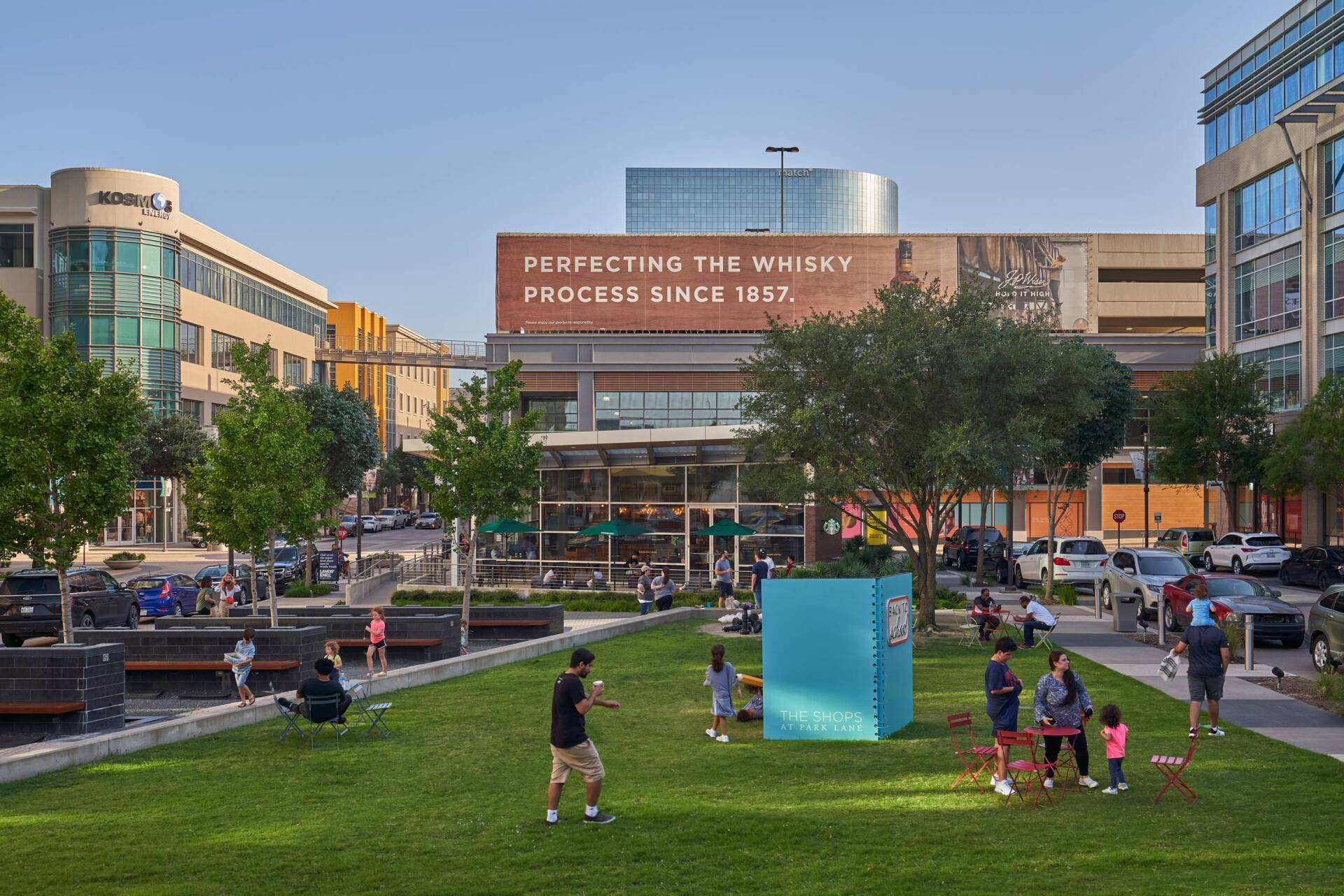 A park with a green lawn and trees, people walking and sitting.