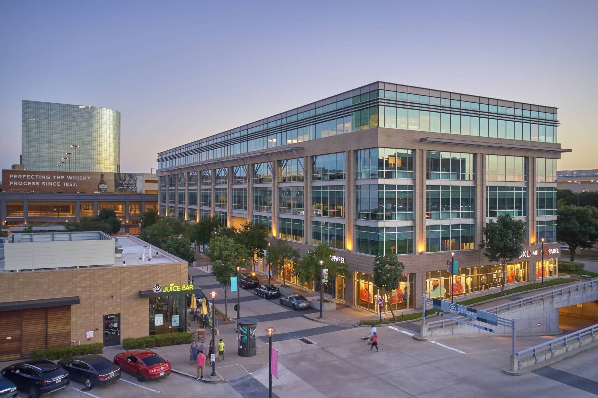 Modern multi-story office building with retail stores below, street, trees, and other buildings.