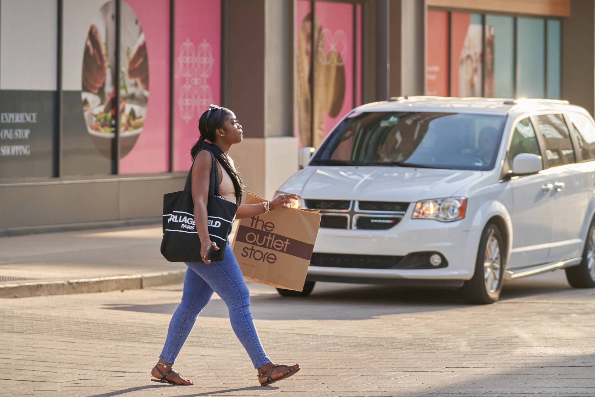 Woman crossing street, holding shopping bag and purse, white van approaching on a city street.