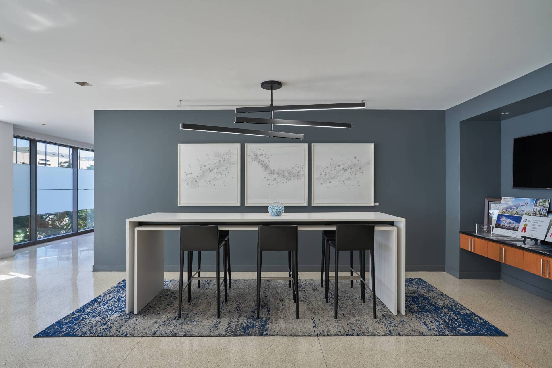 Modern dining area with a long white table, black chairs, and abstract art on a blue wall.