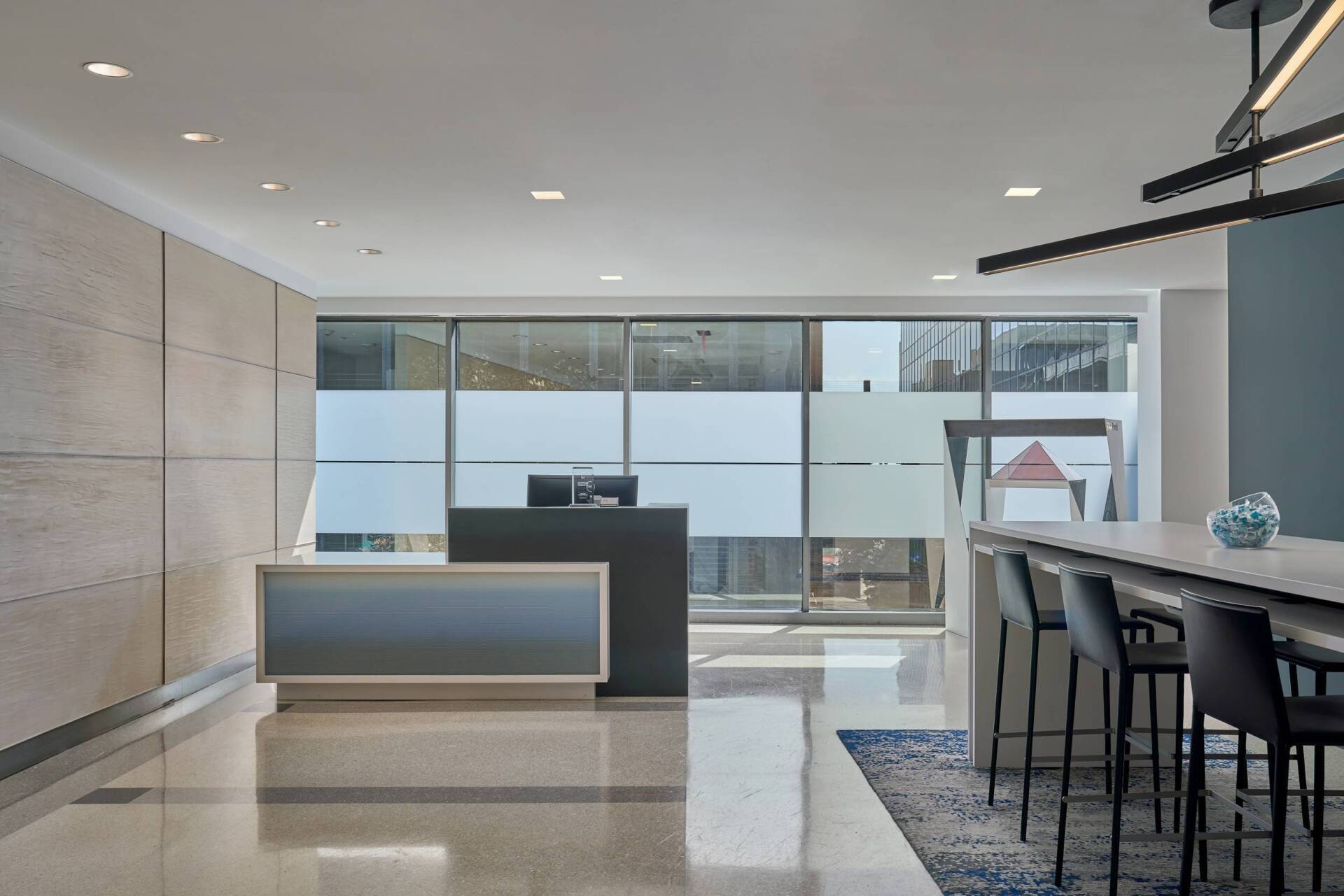 Modern office reception area with counter, bar stools, and large windows.