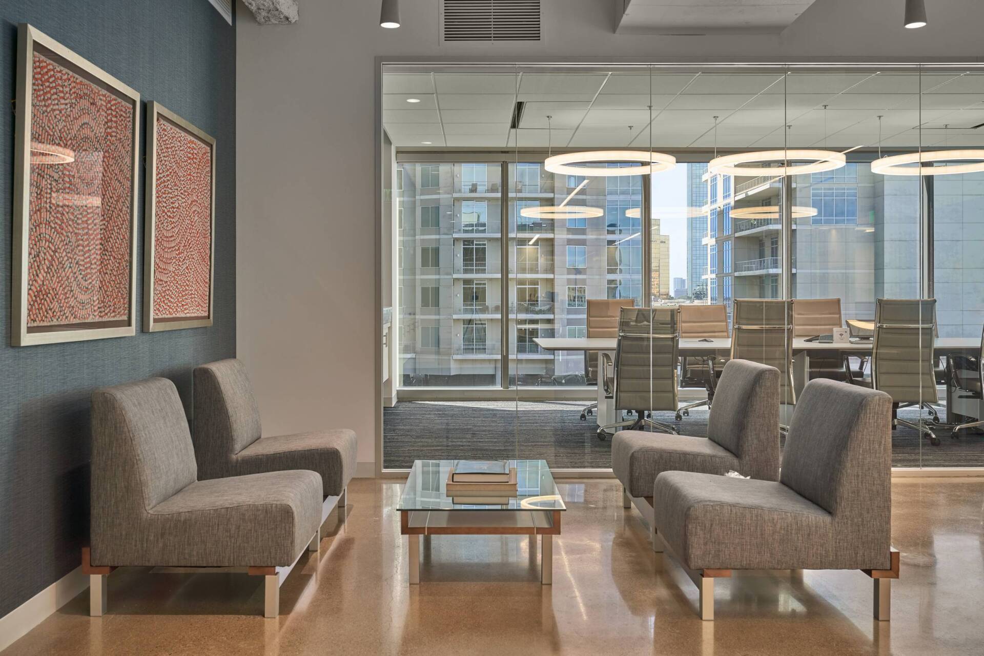 Modern office waiting area with gray couches, glass coffee table, and city view.