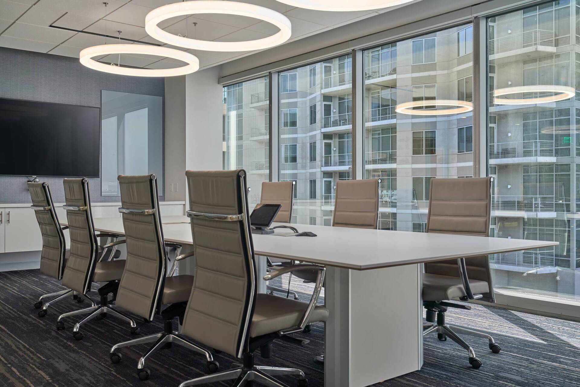 Conference room with long white table, chairs, large windows, and modern light fixtures.