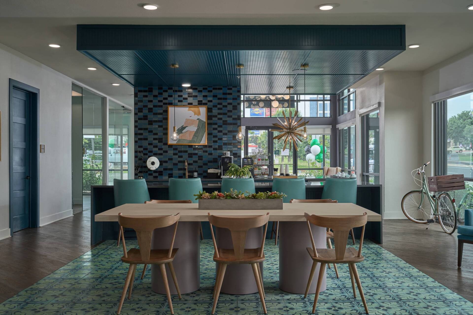 Modern dining area with long table, blue chairs, and teal rug.