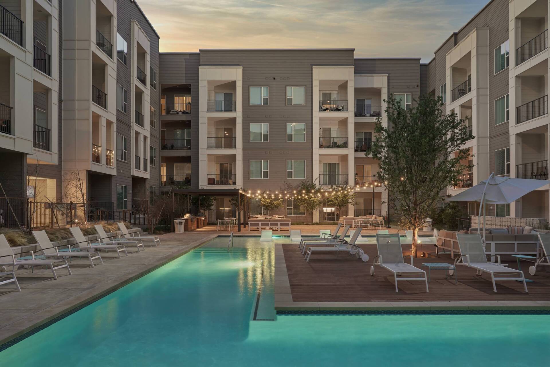 Swimming pool surrounded by apartment buildings with lounge chairs.