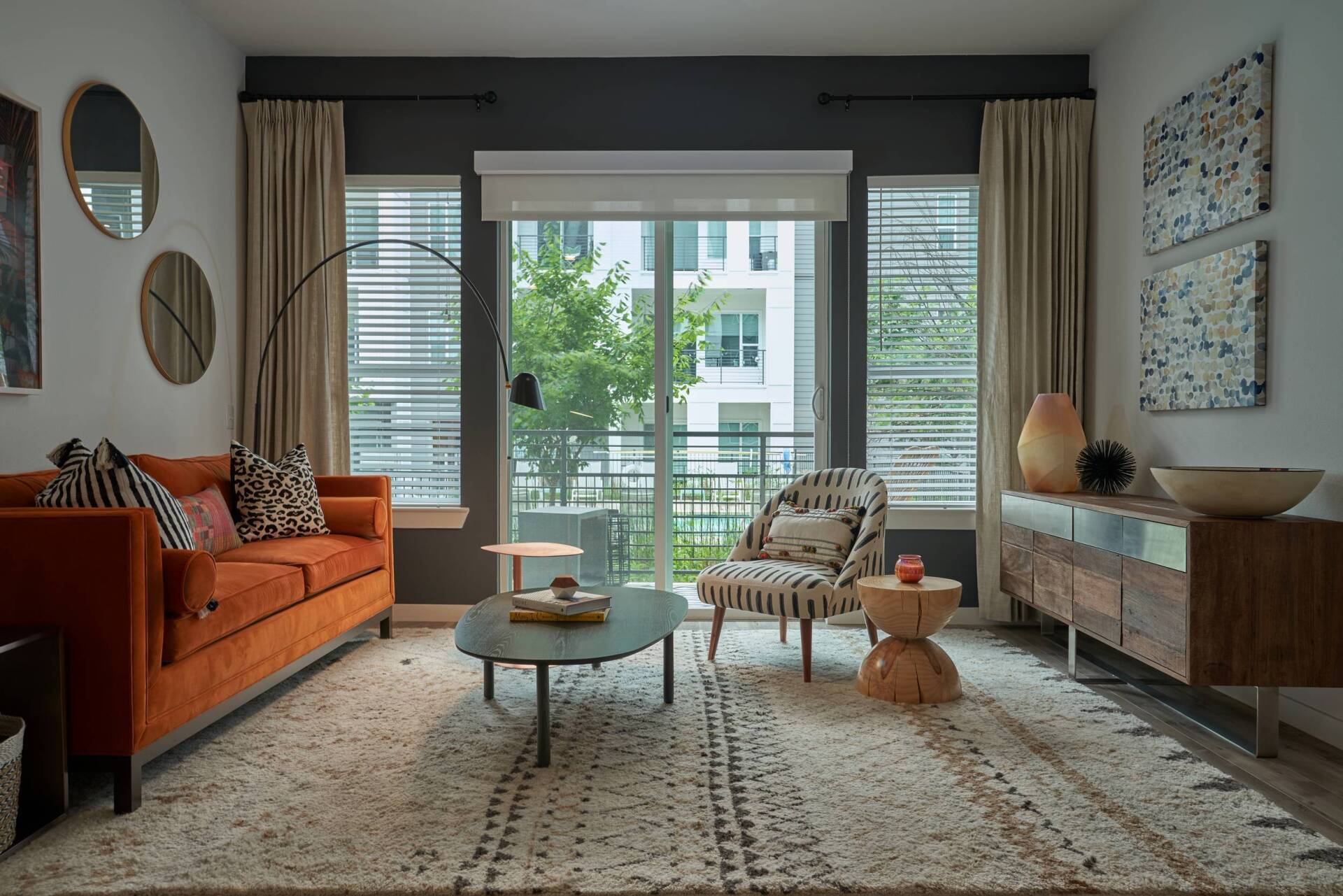 Living room with orange sofa, patterned chair, rug, and dark accent wall, with large window.