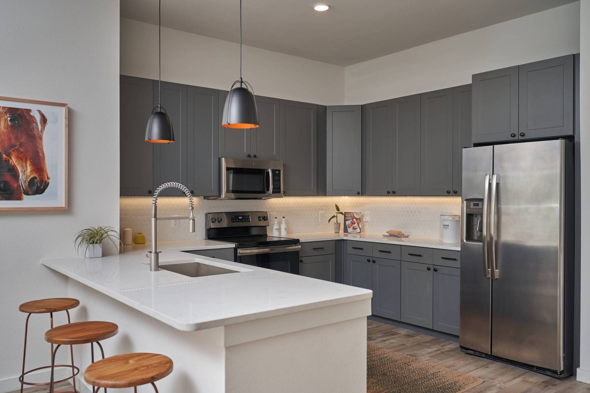 Modern kitchen with gray cabinets, white countertop, stainless steel appliances, and pendant lights.