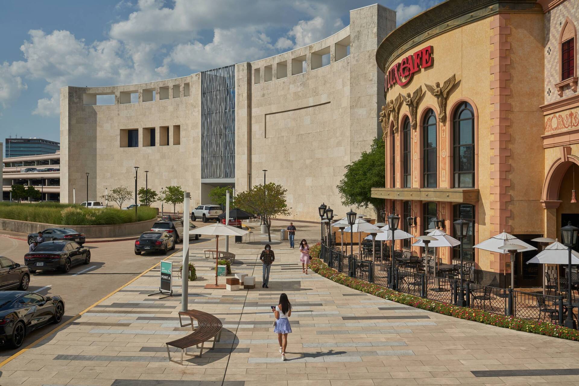 Sidewalk with shoppers and restaurants, a large stone building with a waterfall feature.