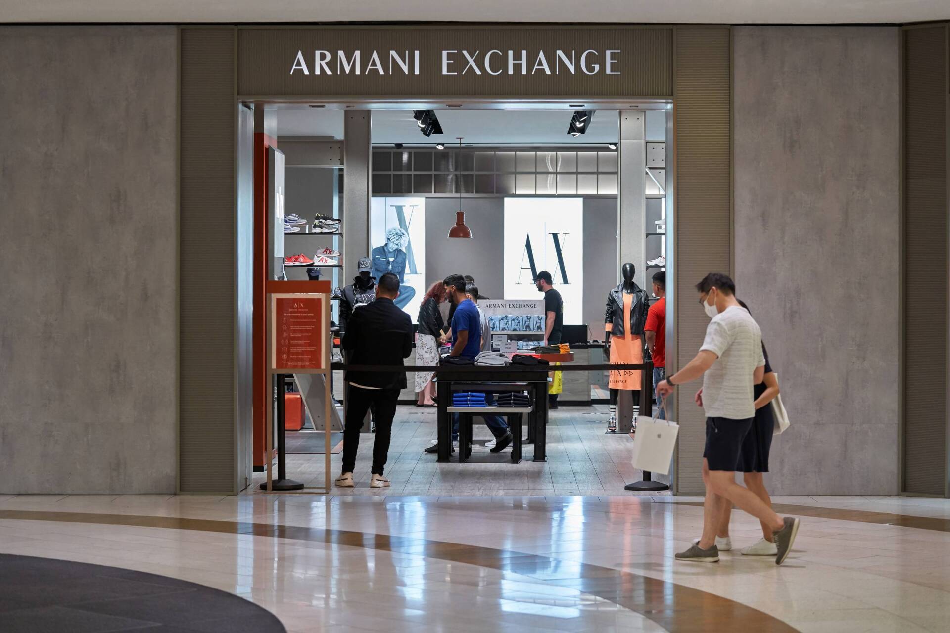 Armani Exchange store entrance in a mall. People enter/exit, and browse inside. Signage visible.