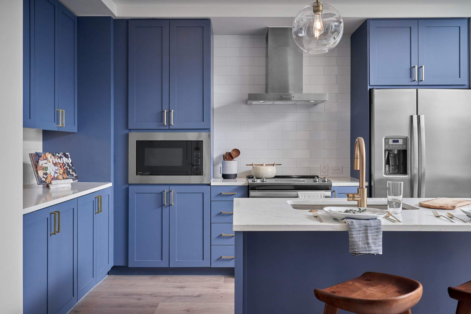 Blue kitchen with white countertops, stainless steel appliances, and a central island with stools.