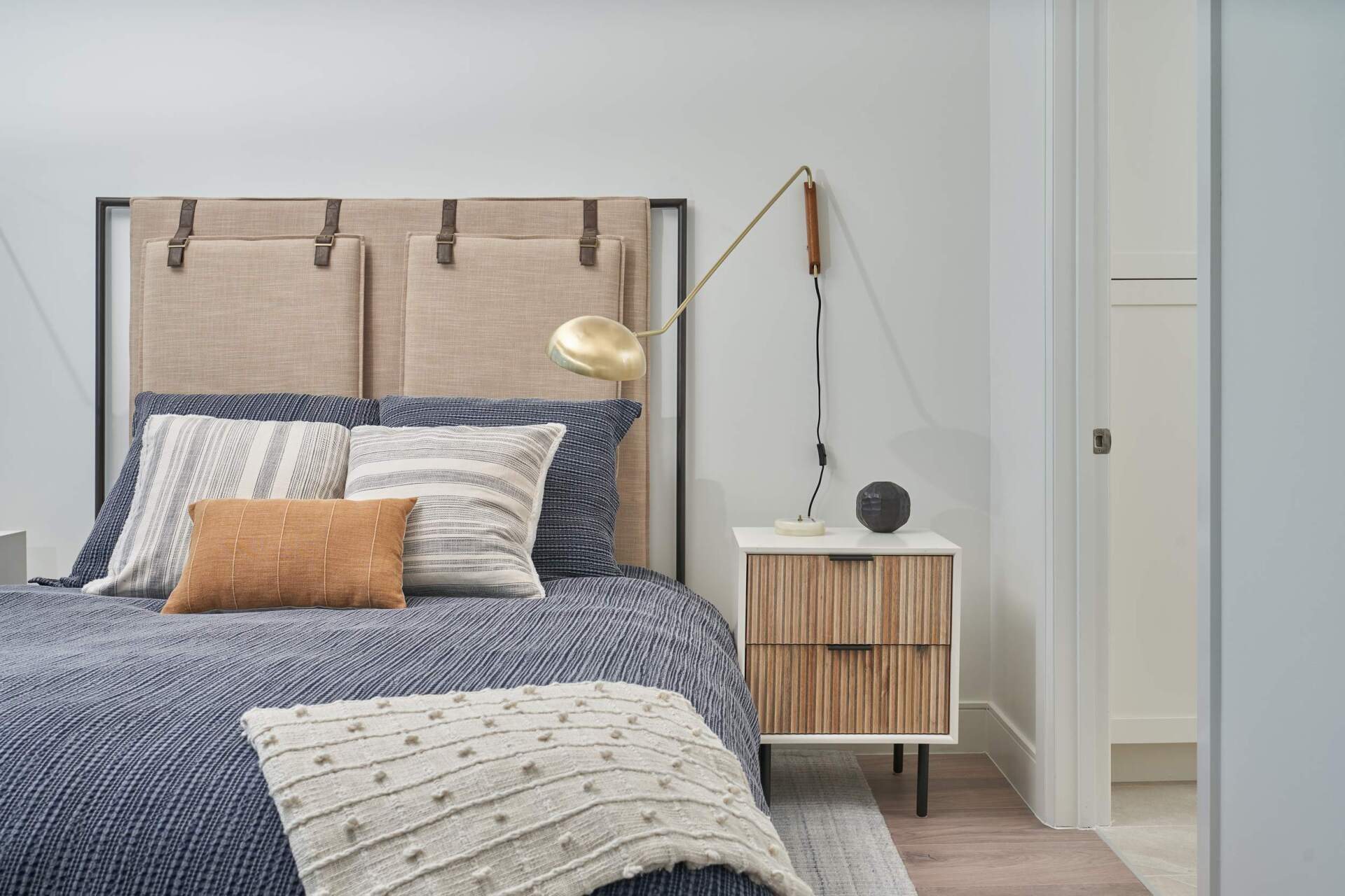 Bedroom with blue bedding, a tan headboard, and a gold and wood bedside lamp.