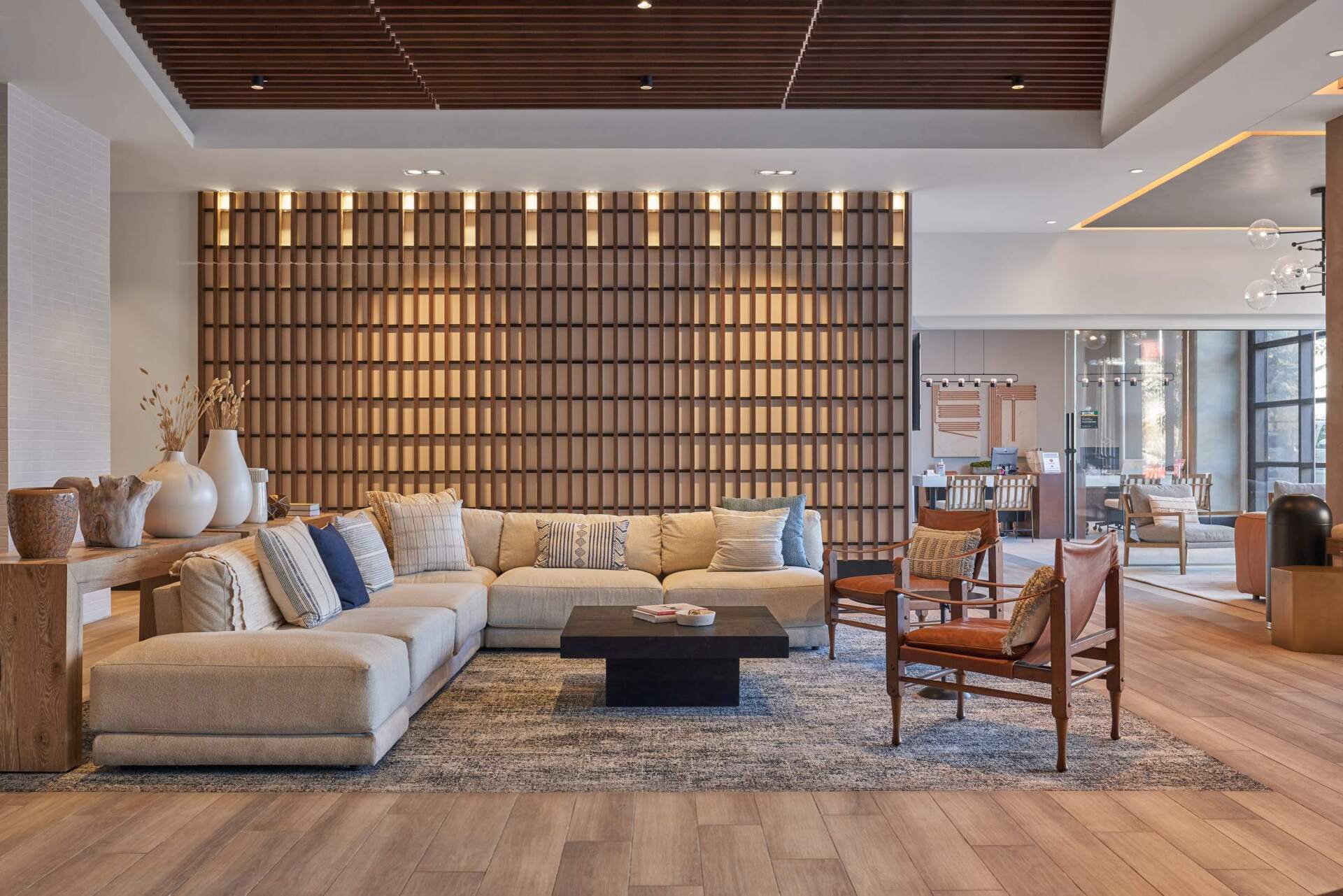 Lounge area with sectional sofa, wooden wall, and chairs. Warm lighting and wood flooring.