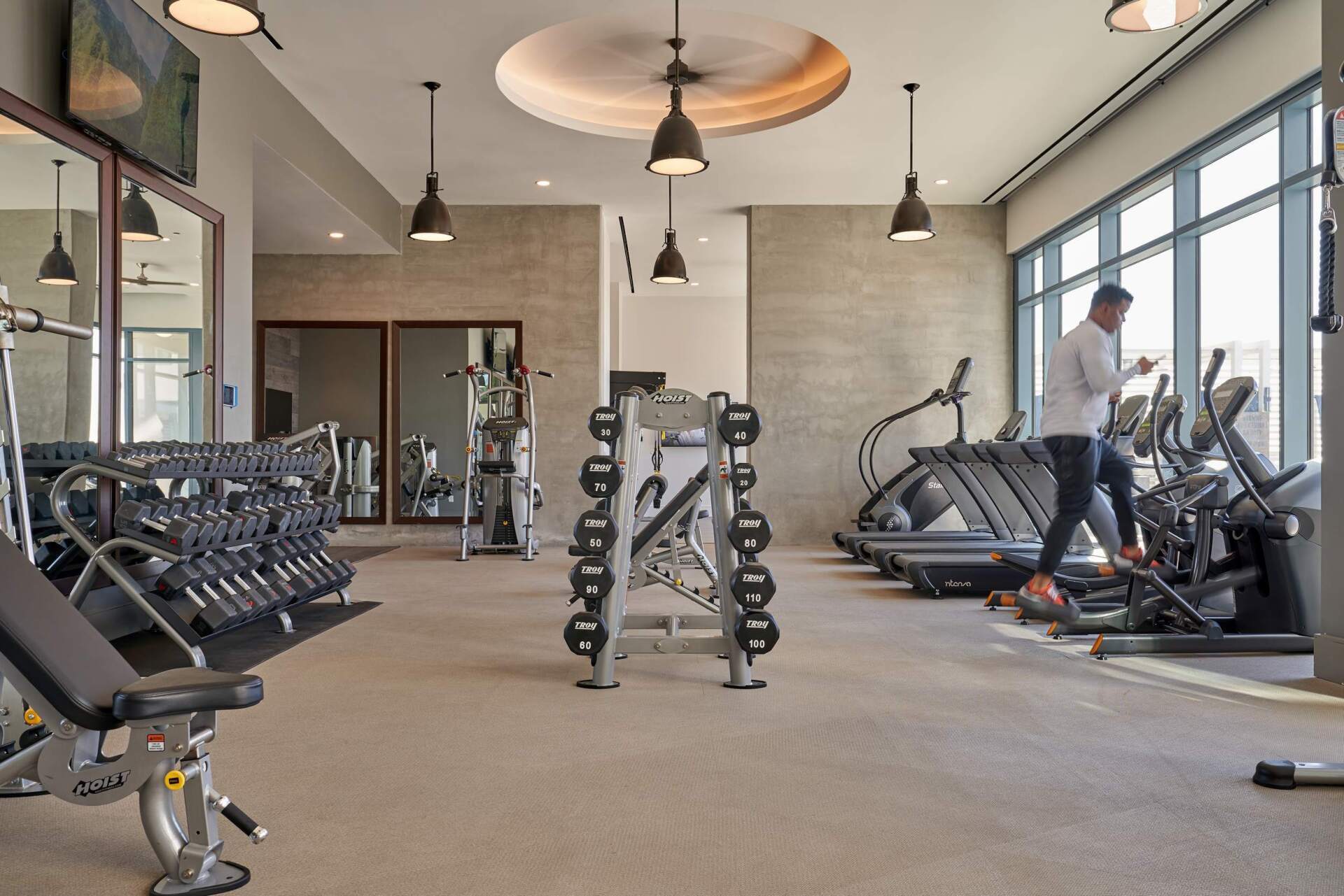 Gym interior with weights, elliptical machines, and person using one.