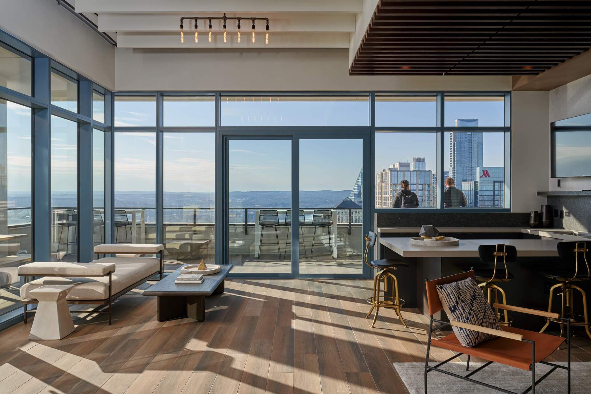 Modern living room with floor-to-ceiling windows, cityscape view, wooden floors, couch.