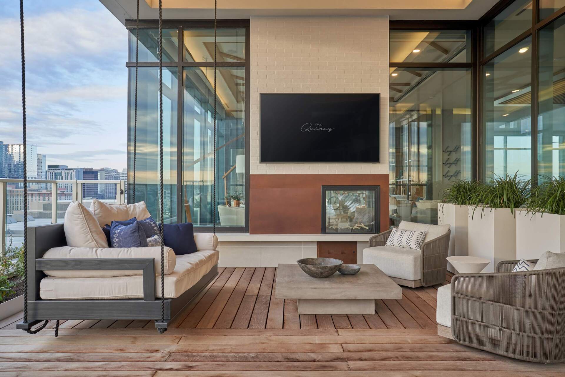 Outdoor patio with seating, swing bed, TV, city views. Wooden deck, neutral tones.