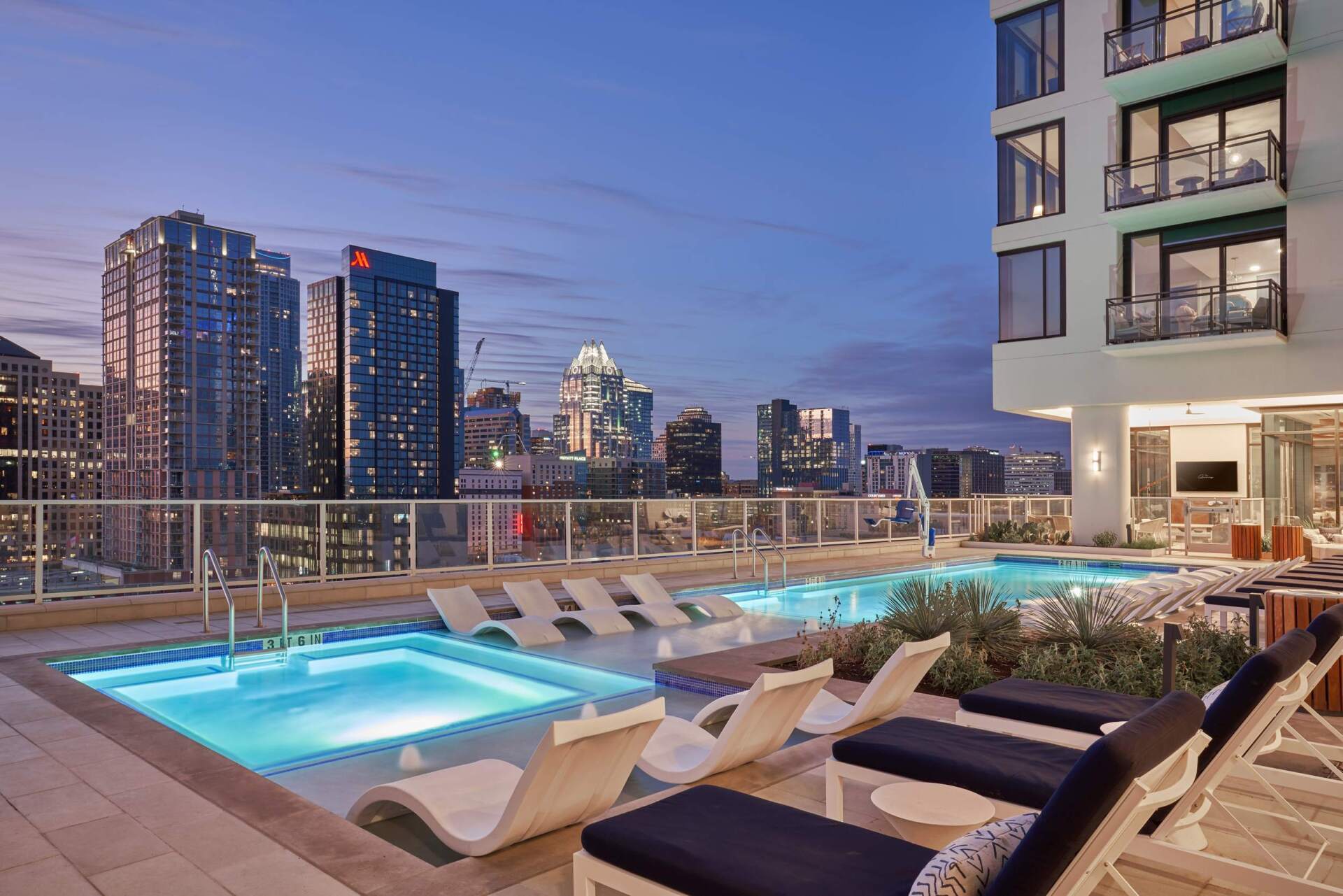 a large swimming pool is surrounded by lounge chairs and a building with a city skyline in the background .