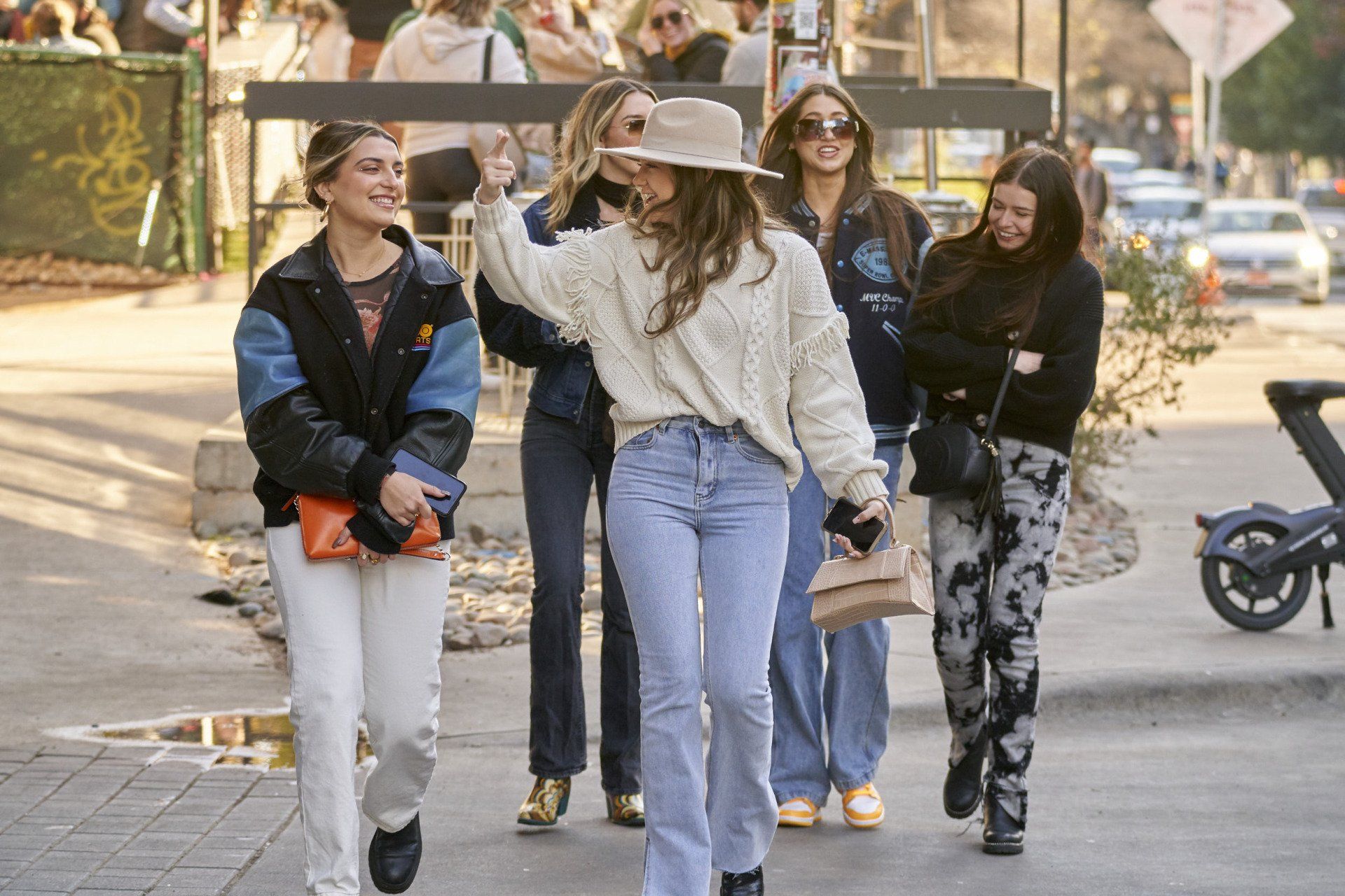 Group of people walking on a city street. One waves, others smile. Sunny day.
