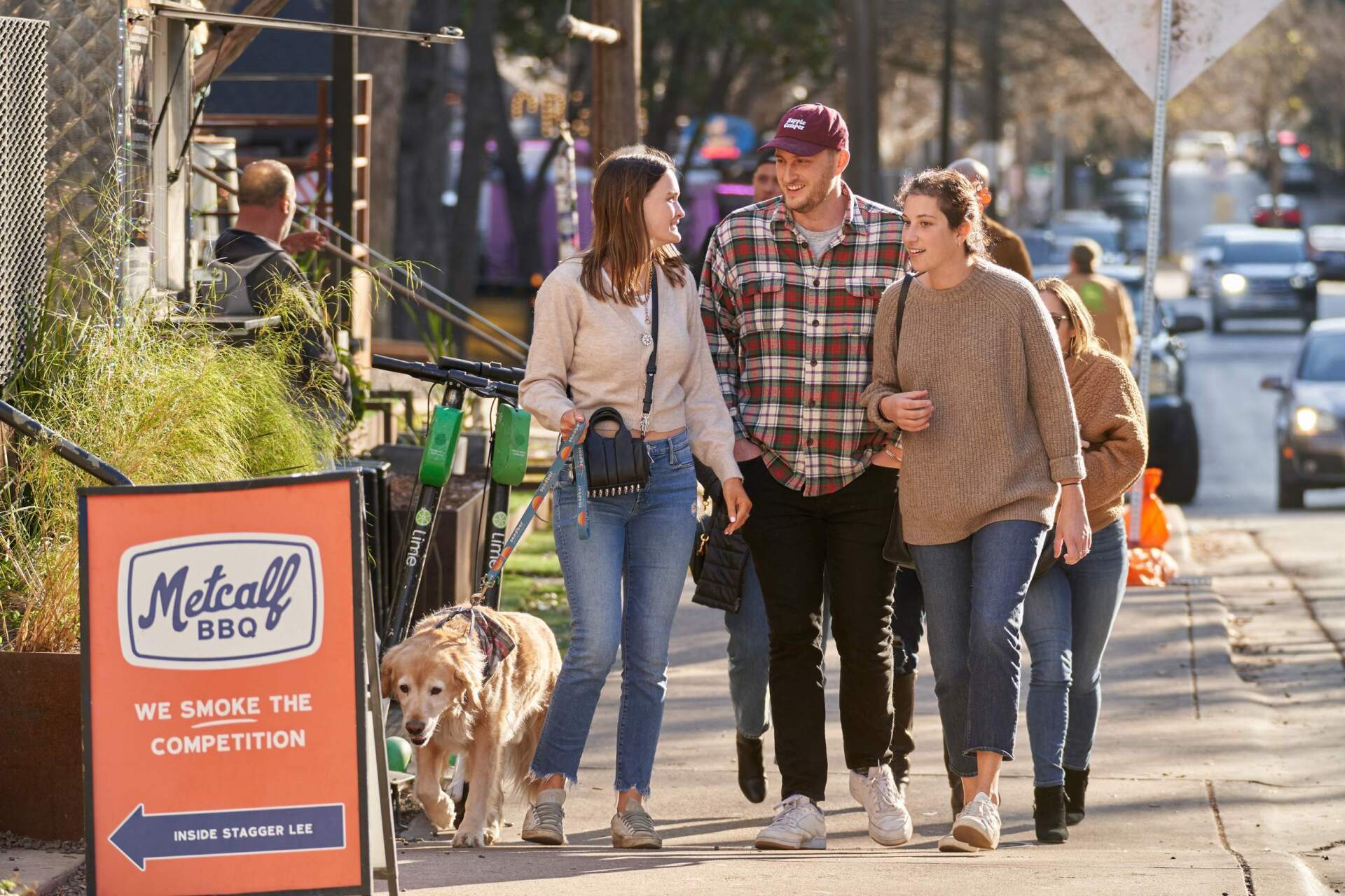 People walking on sidewalk past barbecue restaurant with dog.