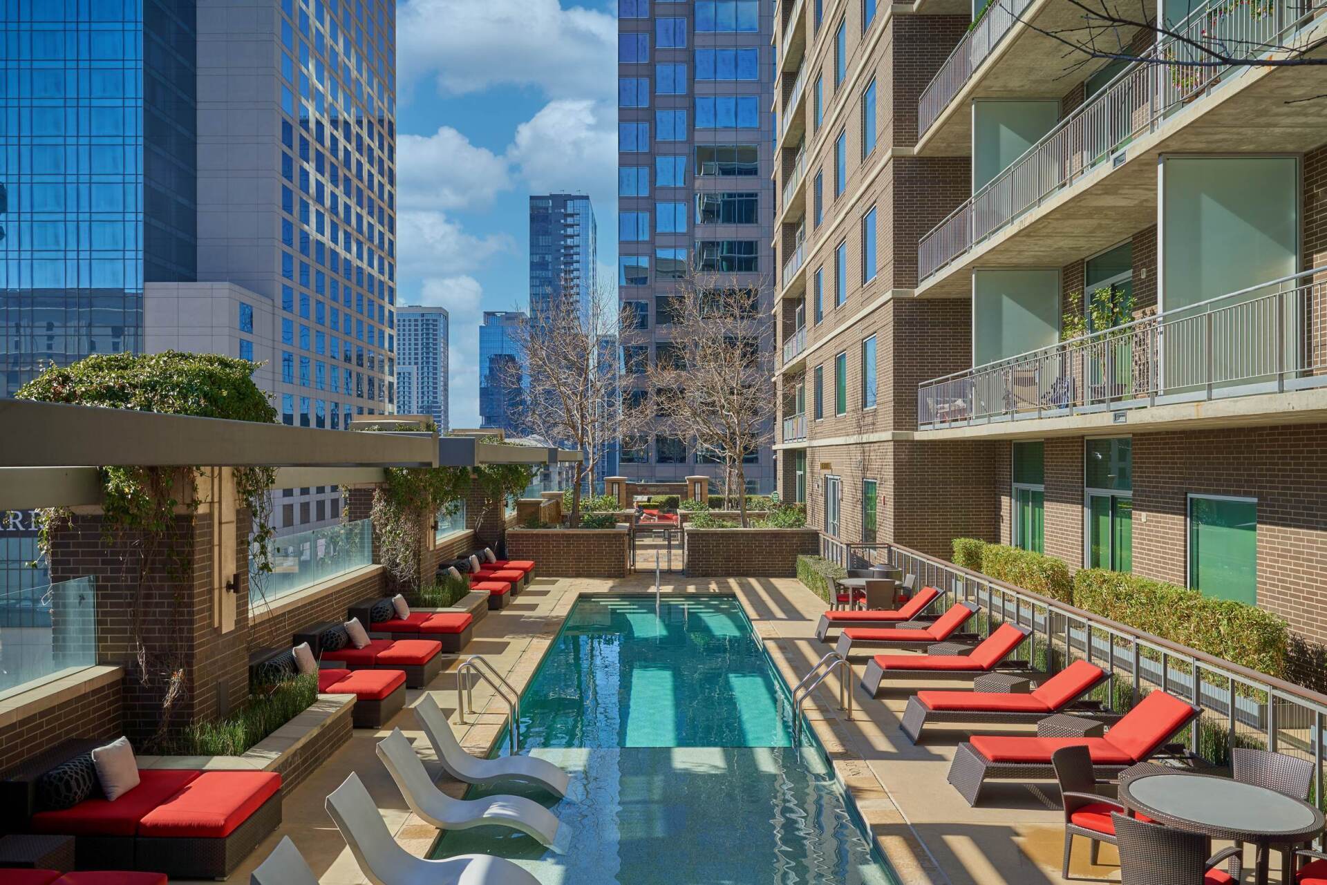 Pool with red lounge chairs and a view of tall city buildings.