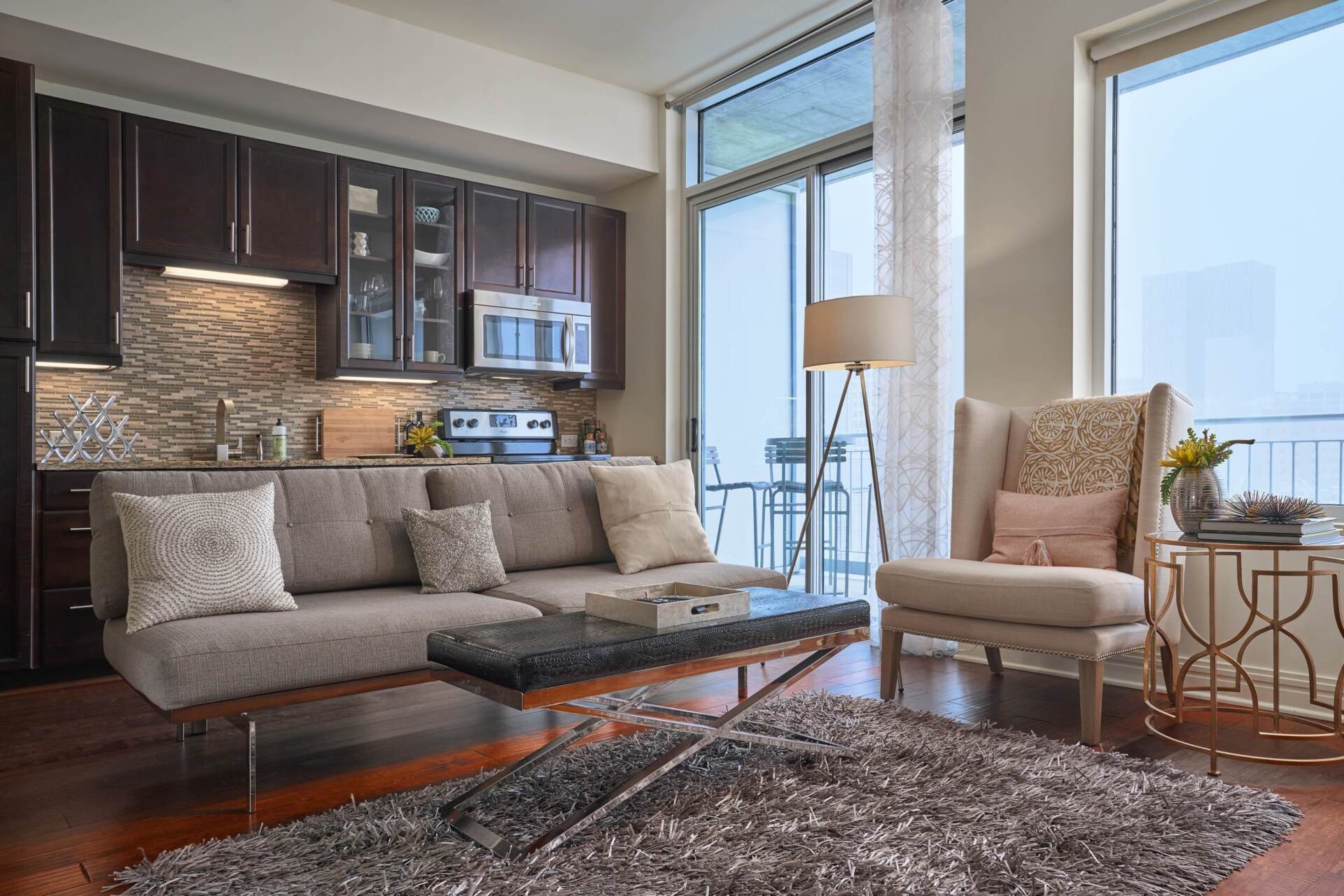 Modern apartment living room with a kitchen, couch, and chair near a window.