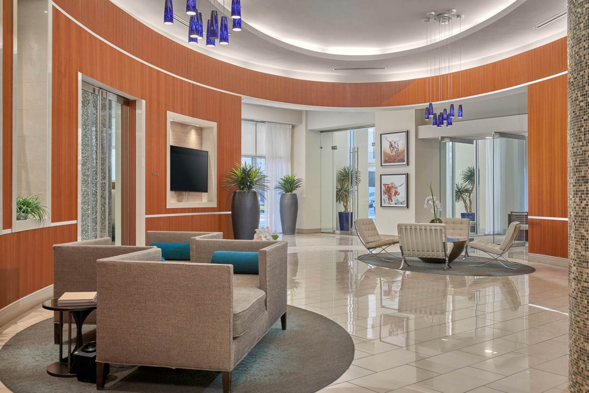 Lobby with curved wood-paneled walls, marble floors, and seating areas. Blue and neutral tones.