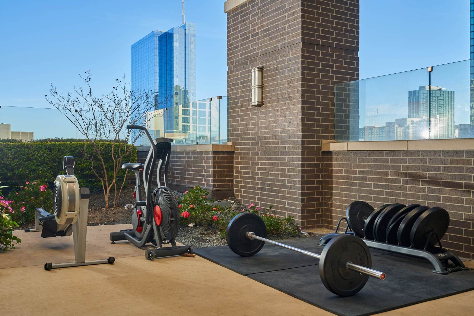Rooftop gym with cardio and weight equipment, brick walls, and city skyline.