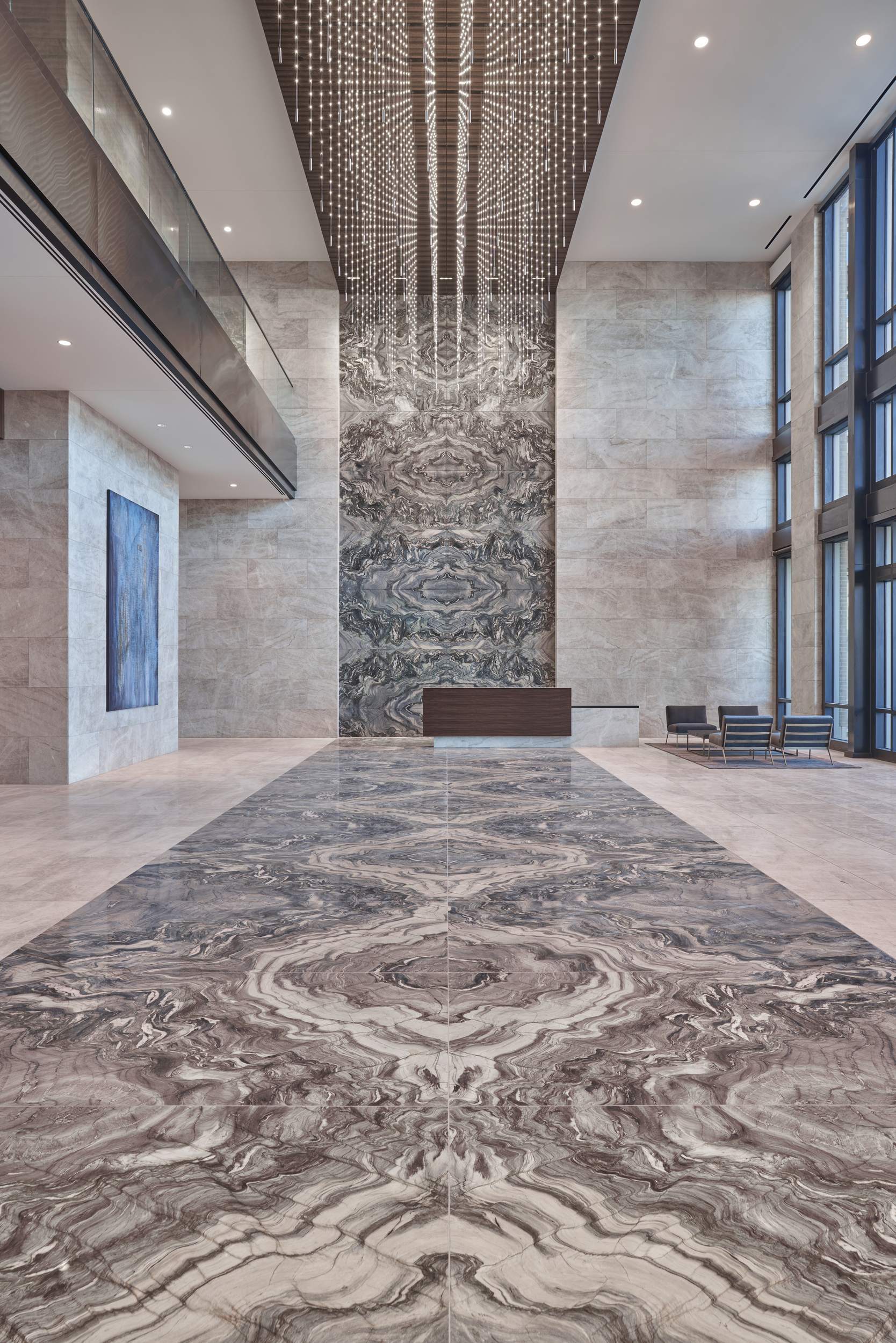 Spacious lobby with marble floor, tall walls, and a large chandelier. Reception desk and seating in the distance.