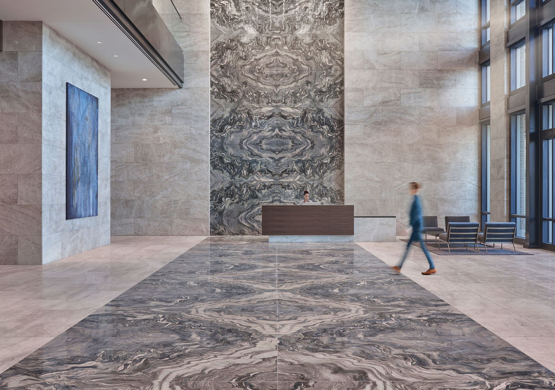 Modern lobby with large marble wall, patterned floor, reception desk, and person walking.