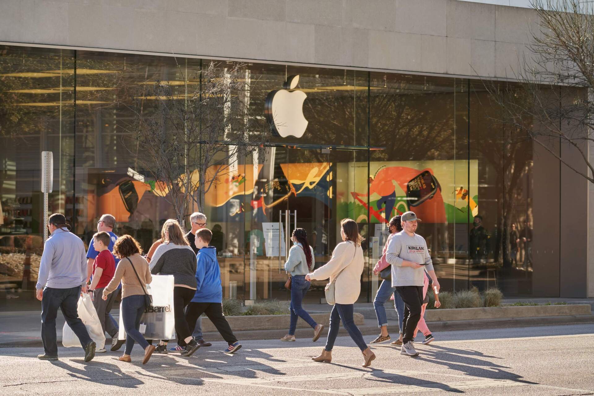 People crossing the street in front of an Apple store with a large apple logo.