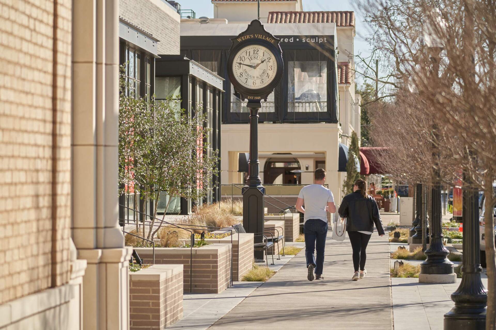 People walking on a brick sidewalk with a clock tower and buildings. Sunny day.