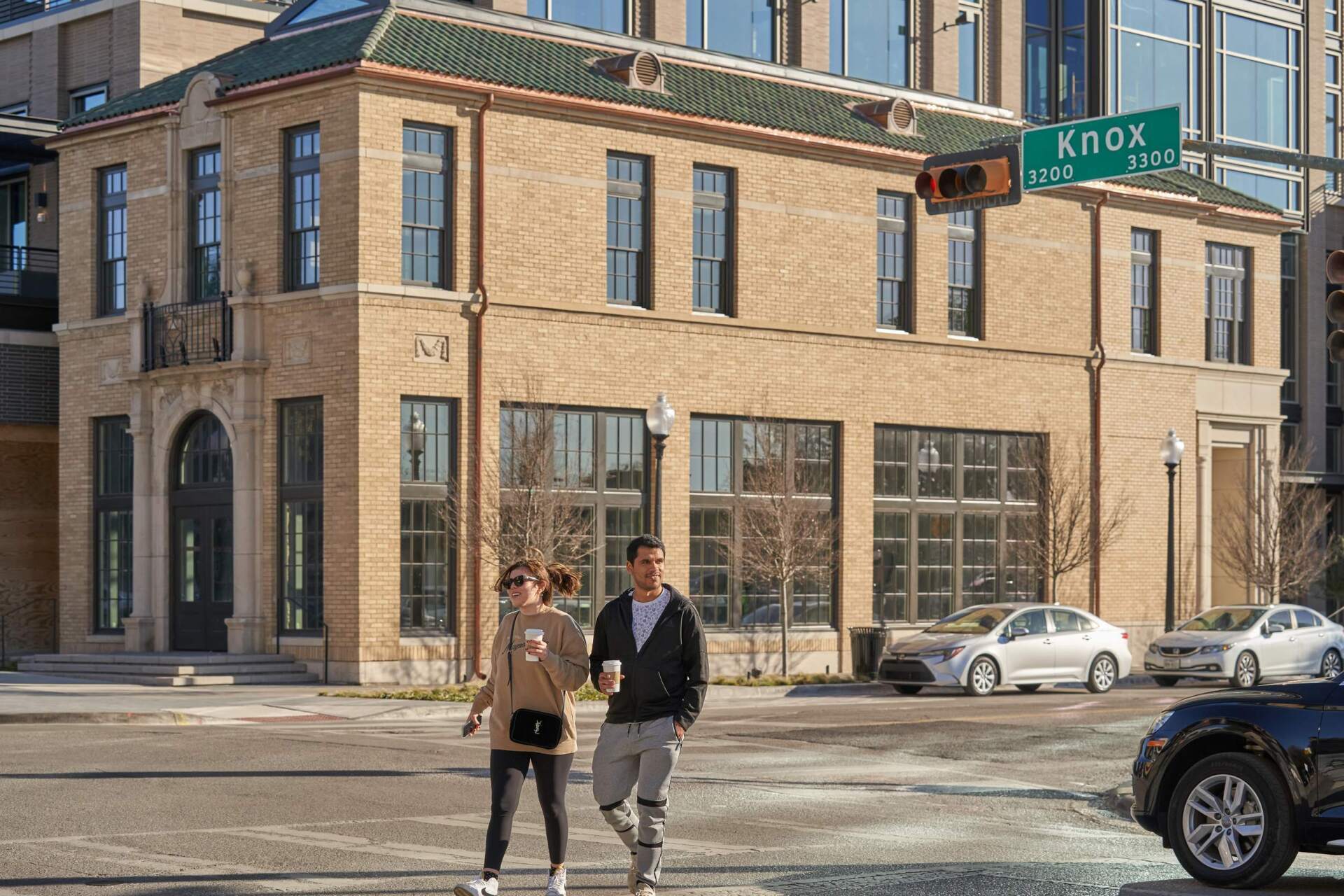 Couple crossing street in front of a brick building. Street sign reads 