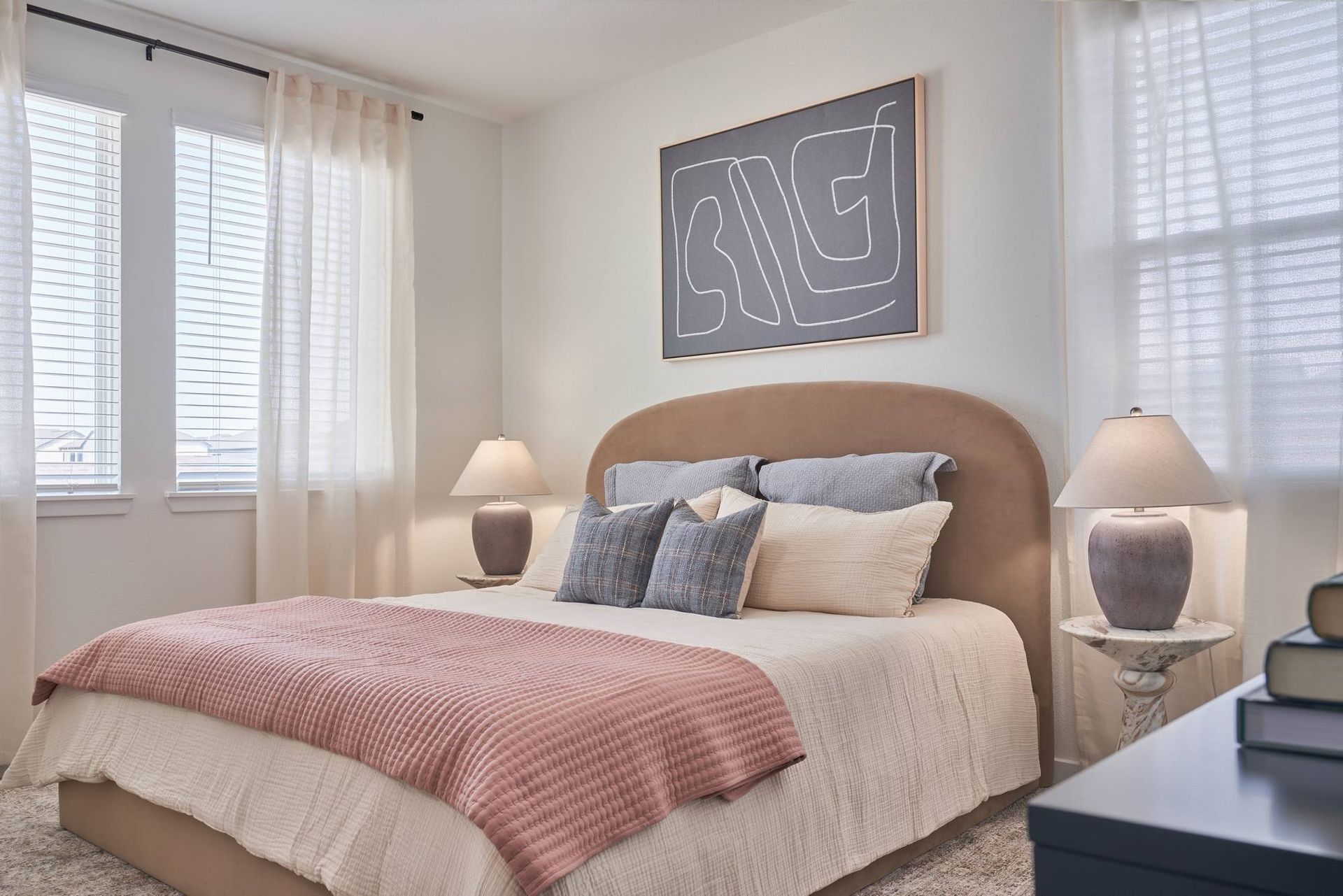Bedroom with bed, art, two windows, two lamps on nightstands, and a desk.