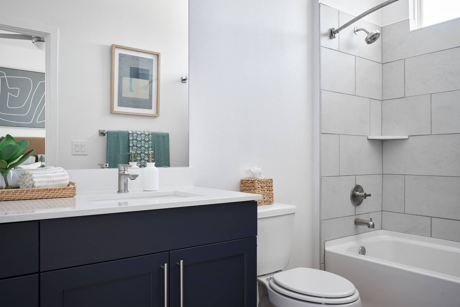 Bathroom with navy vanity, white countertop, white tile shower, and framed artwork.