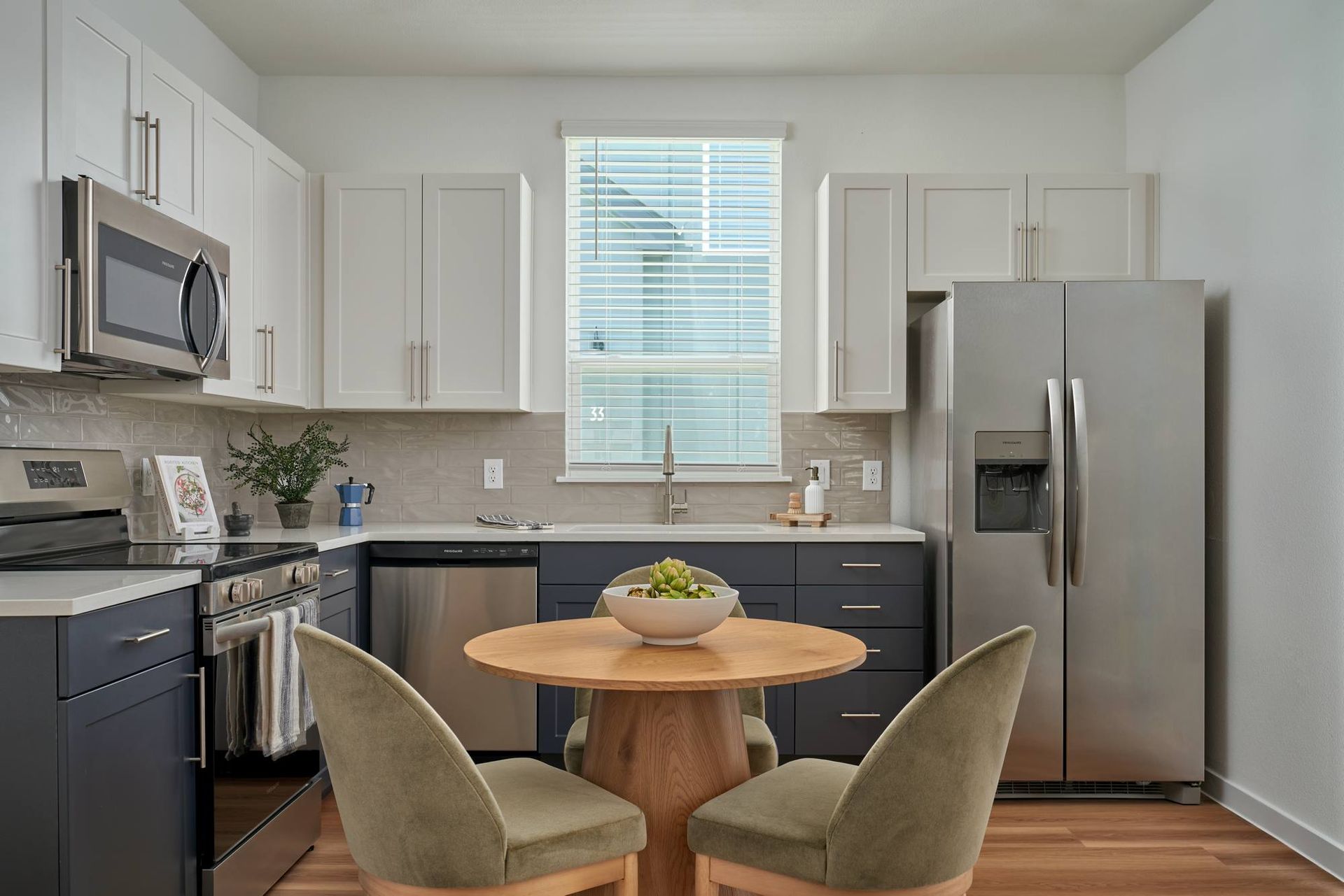 Modern kitchen with stainless steel appliances, dark blue and white cabinets, small wooden table with chairs.