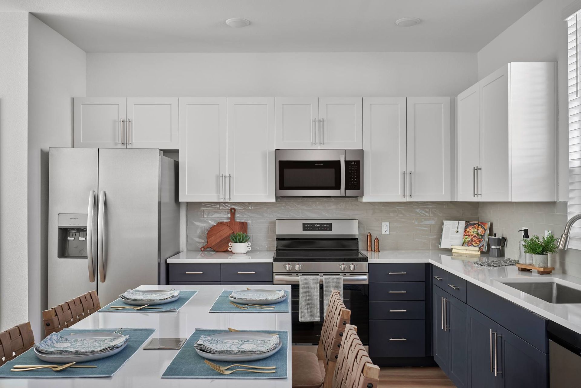 Modern kitchen with white and blue cabinets, stainless steel appliances, and a dining table set for a meal.