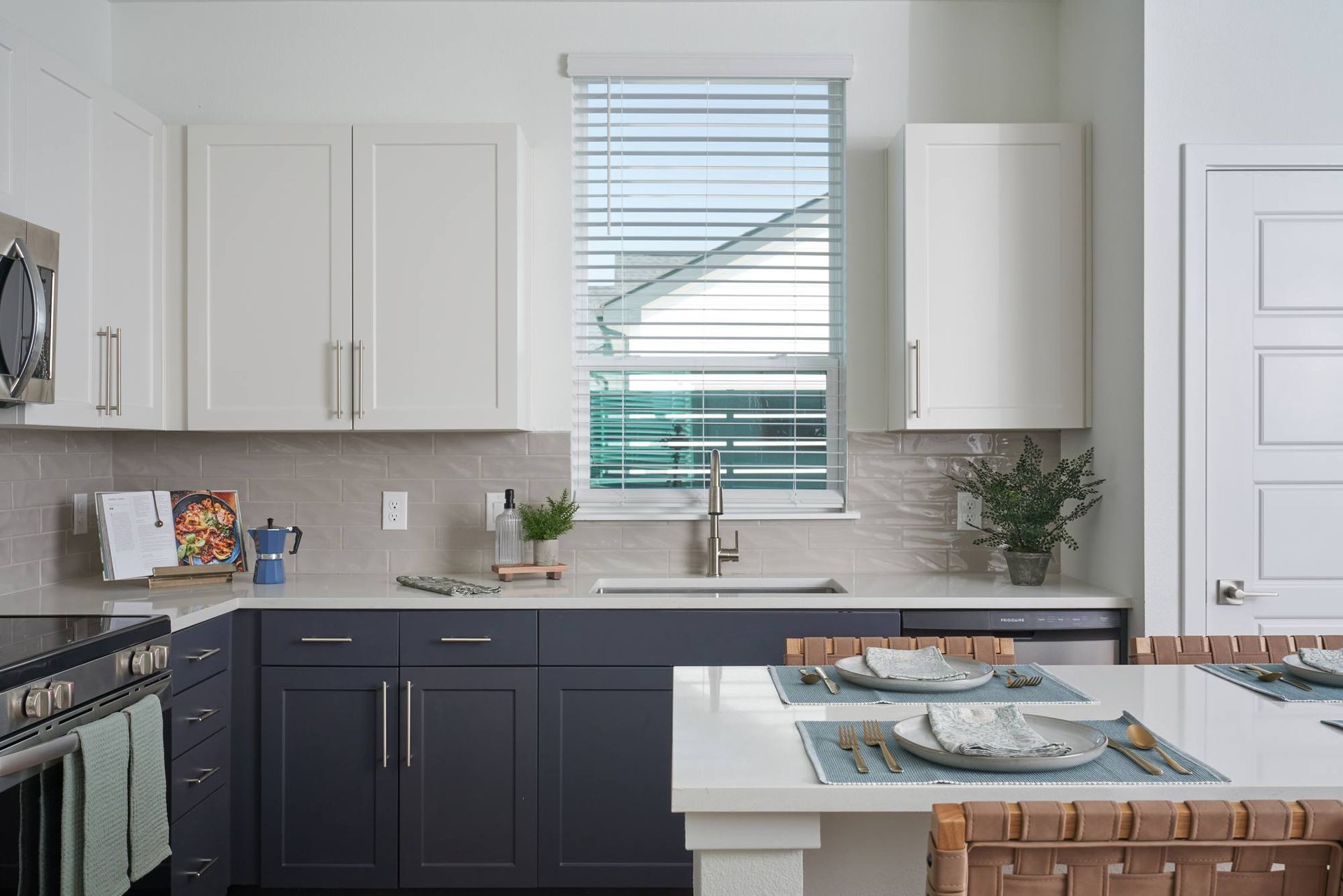 Modern kitchen with white and dark gray cabinets, stainless steel appliances, and a window.