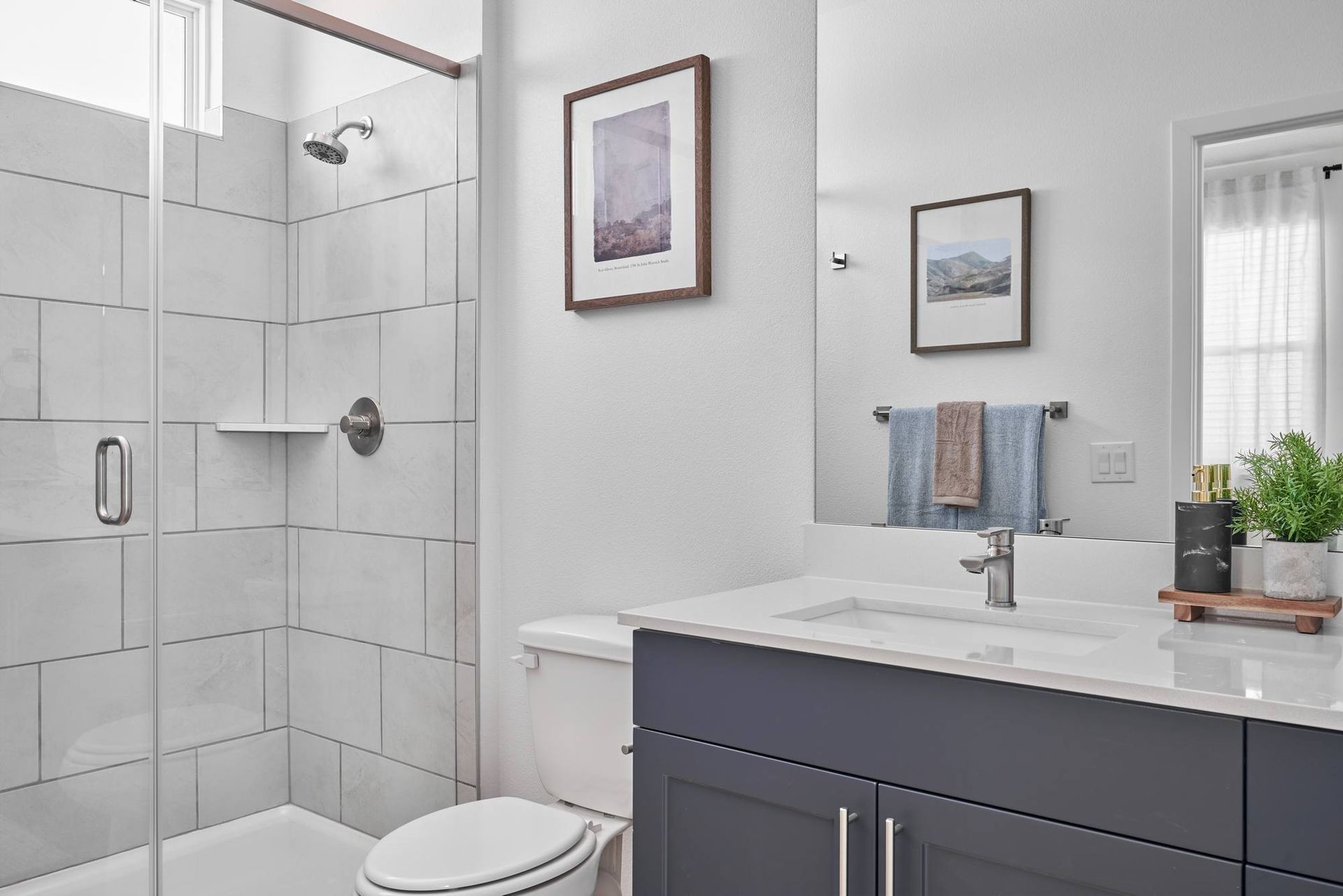 Modern bathroom with a glass-enclosed shower, vanity with a dark blue cabinet, and artwork.