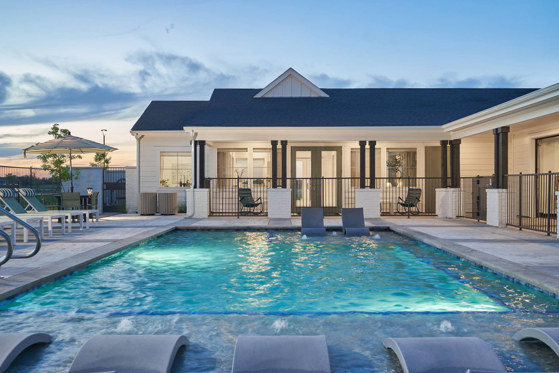 Swimming pool with lounge chairs, white building, and dusk sky.