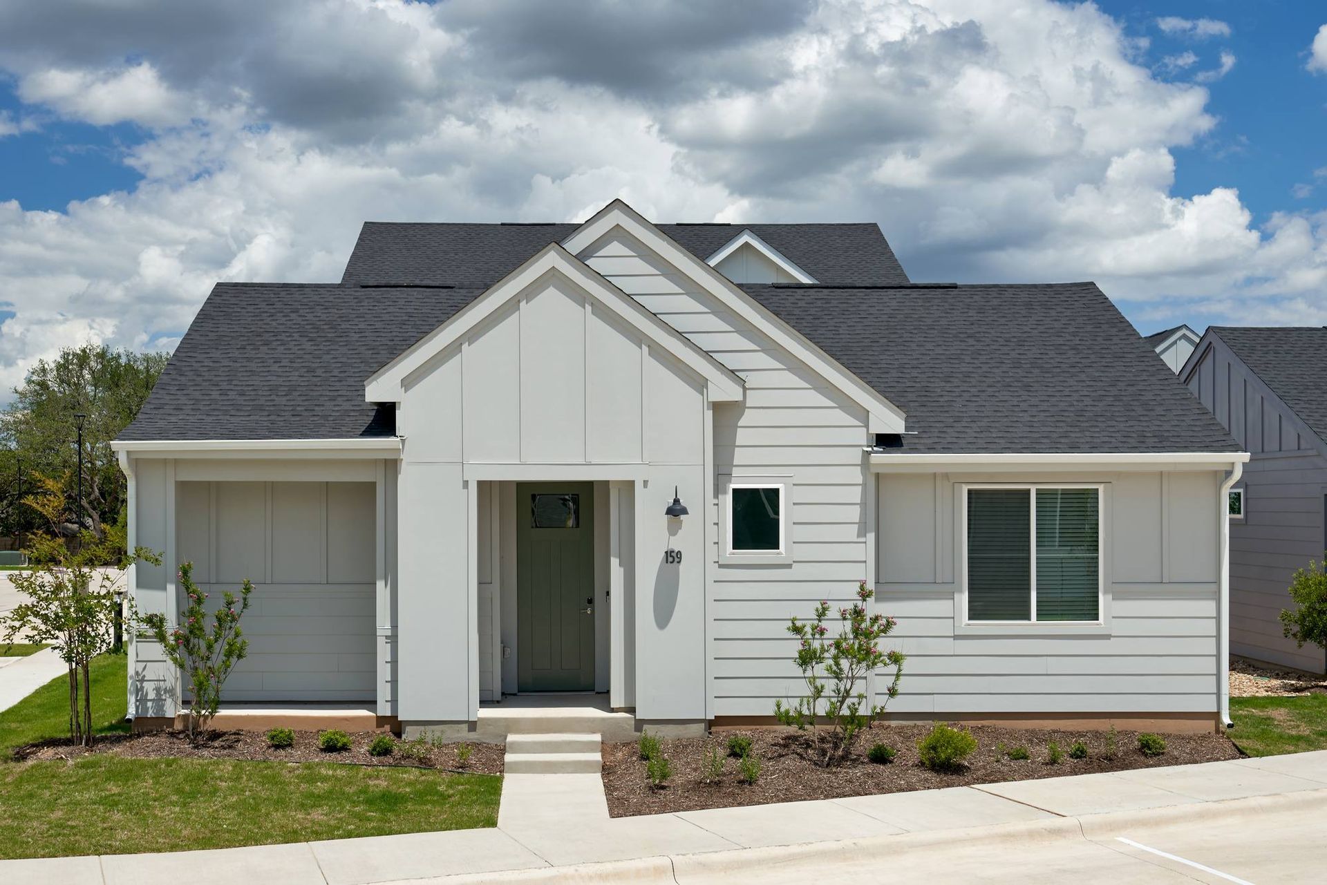 Light gray house with black roof, small front yard, and blue sky.